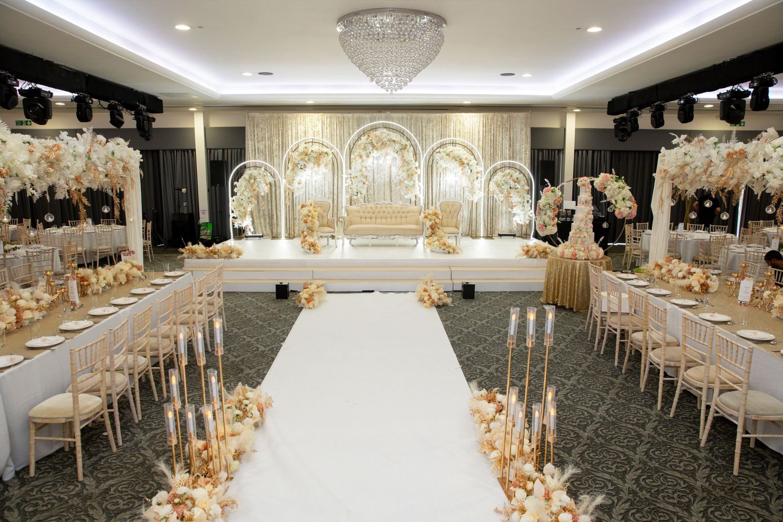 The empty hall before guests arrive, white aisle running to the flowered stage