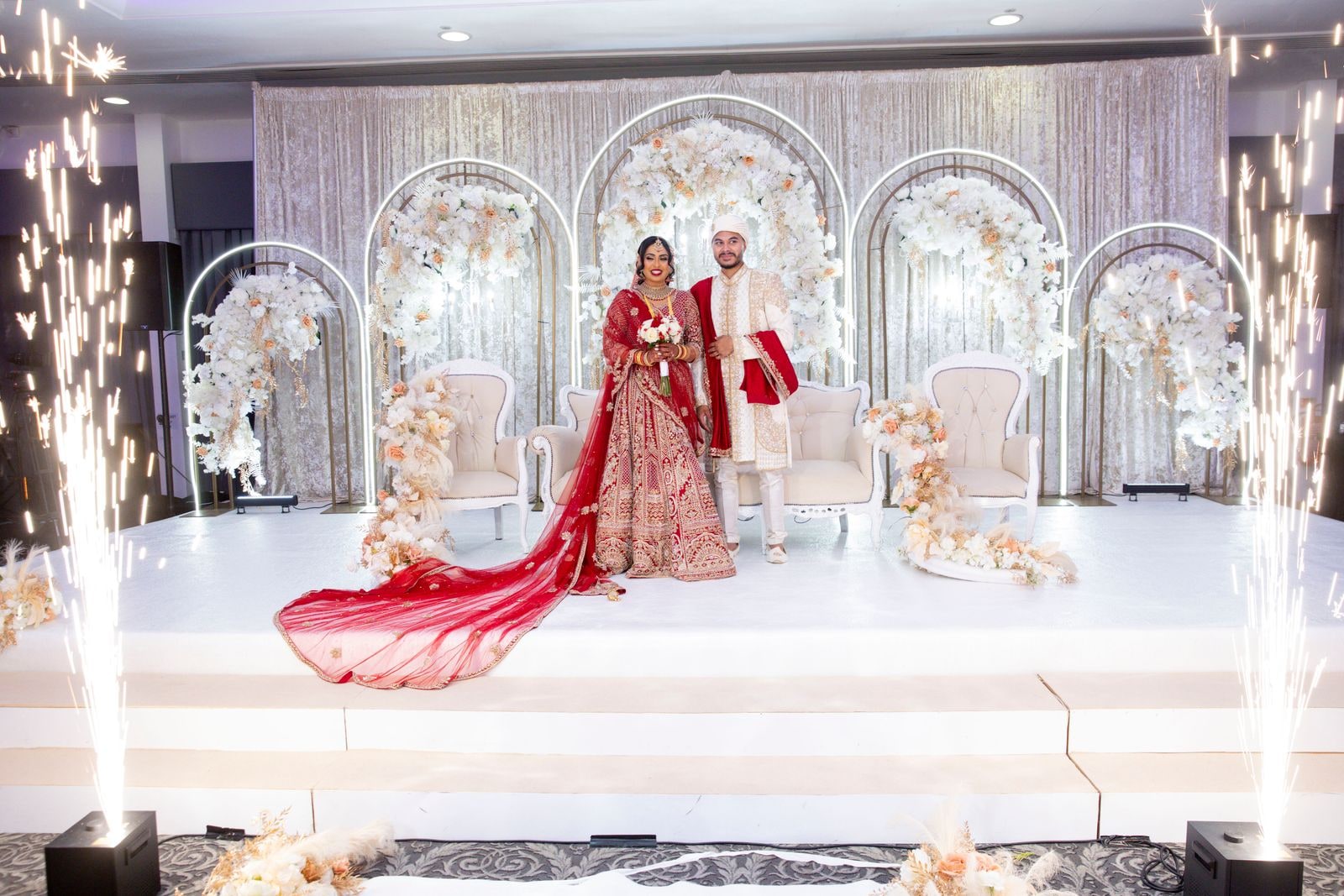 Couple on the stage between fountains of sparks, her red train stretched across the floor