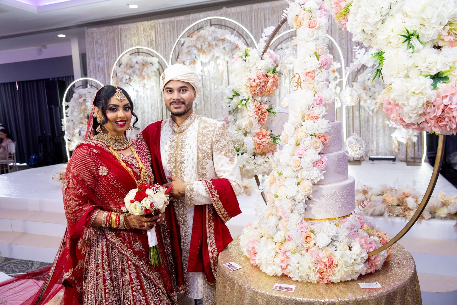 Bride and groom beside the tiered cake in its ring of pale flowers