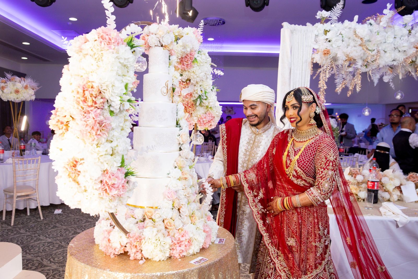 Couple cutting the cake together under a canopy of hanging blossom