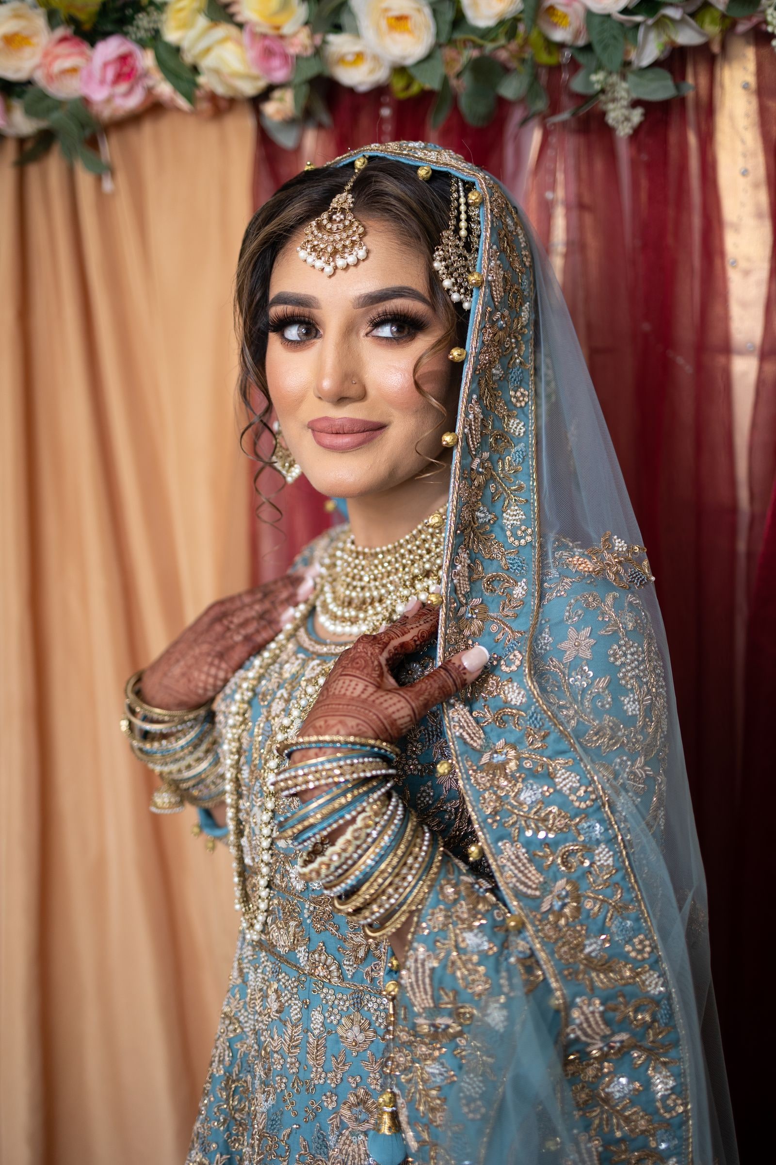 Bride in blue and gold with her hand at her chest, hennaed and heavy with bangles