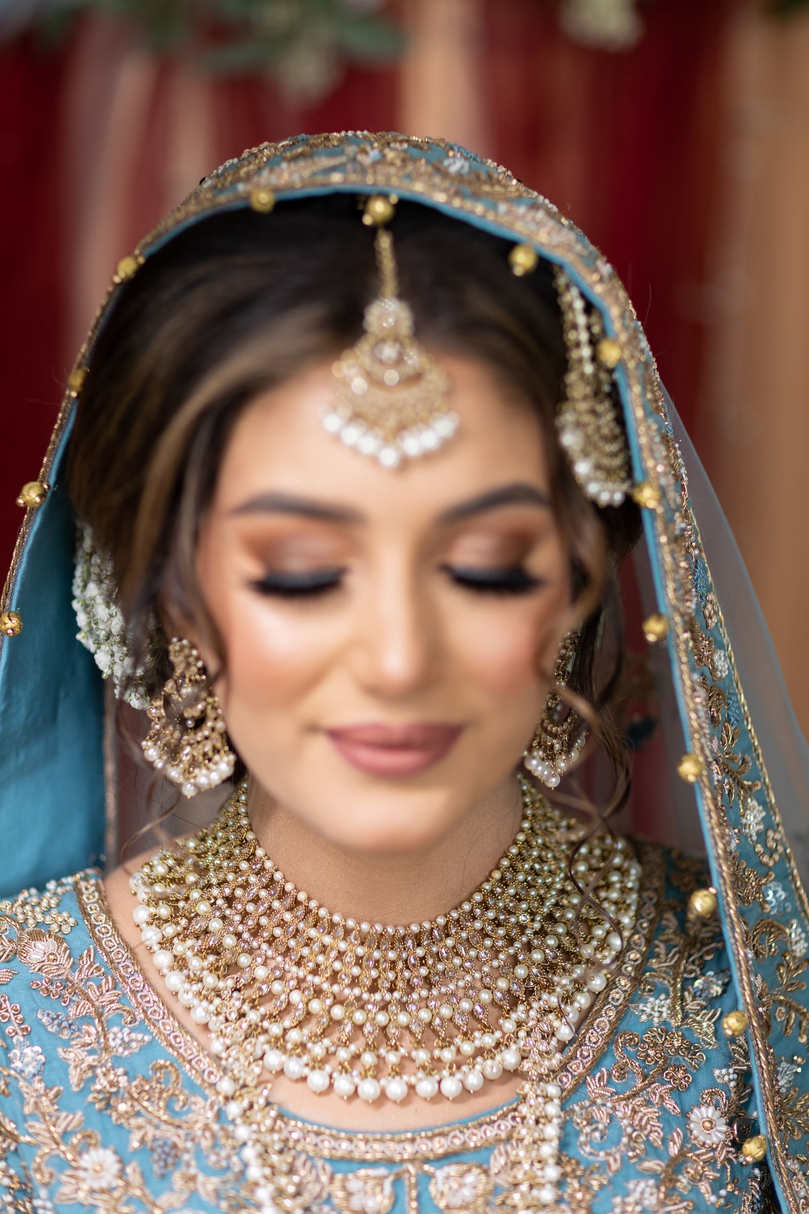 Close portrait of the bride, eyes lowered, in a gold tikka and layered pearl necklaces