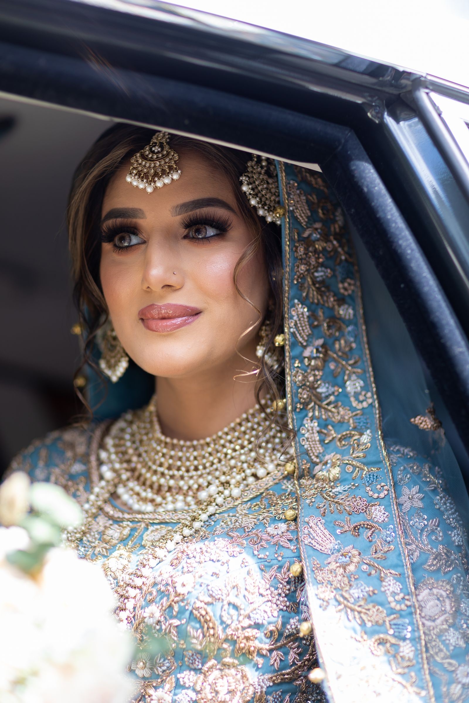 Bride looking out through a car window in blue and gold, holding white flowers