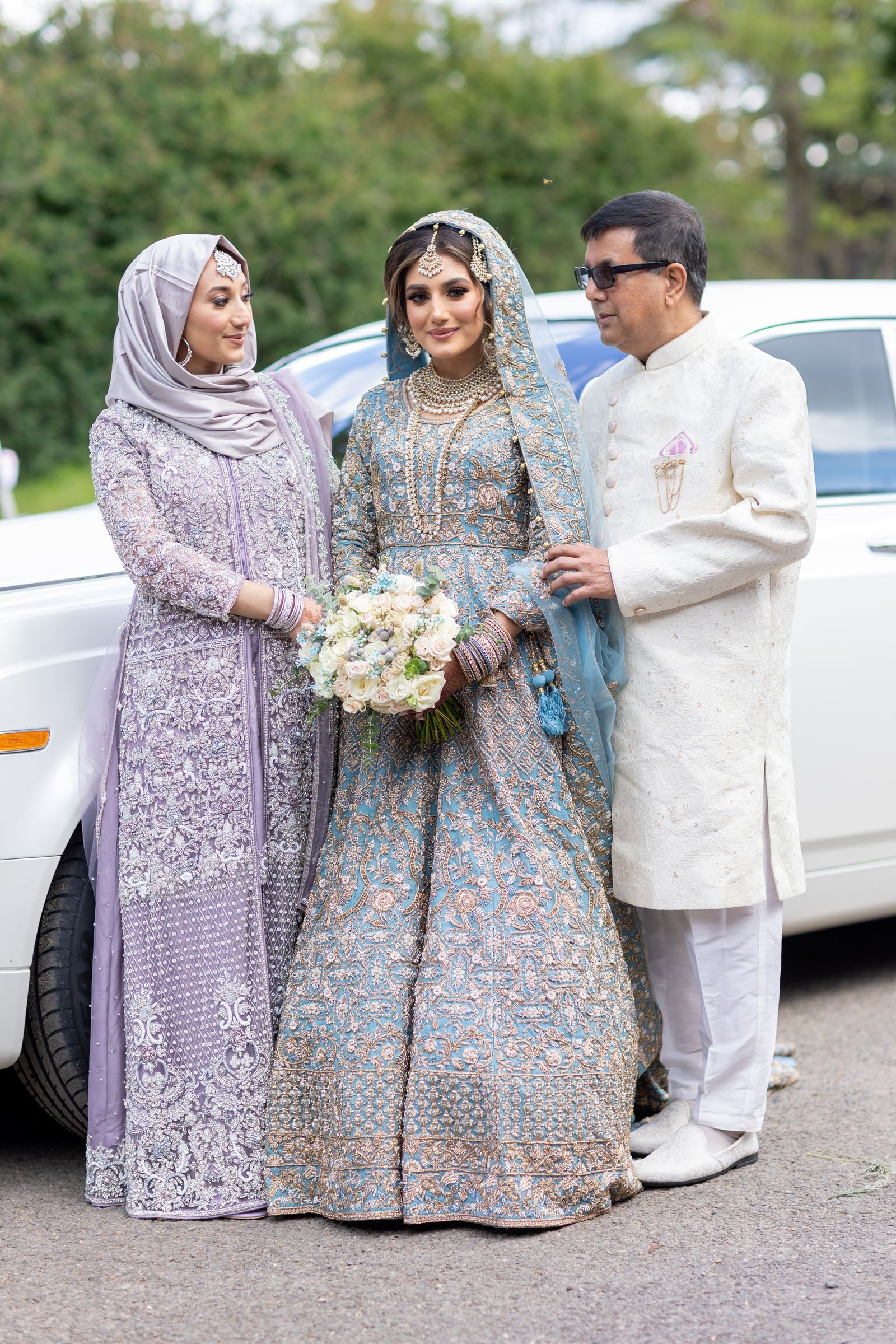 Bride with her parents beside the car, her father in an ivory kurta, her mother in lilac