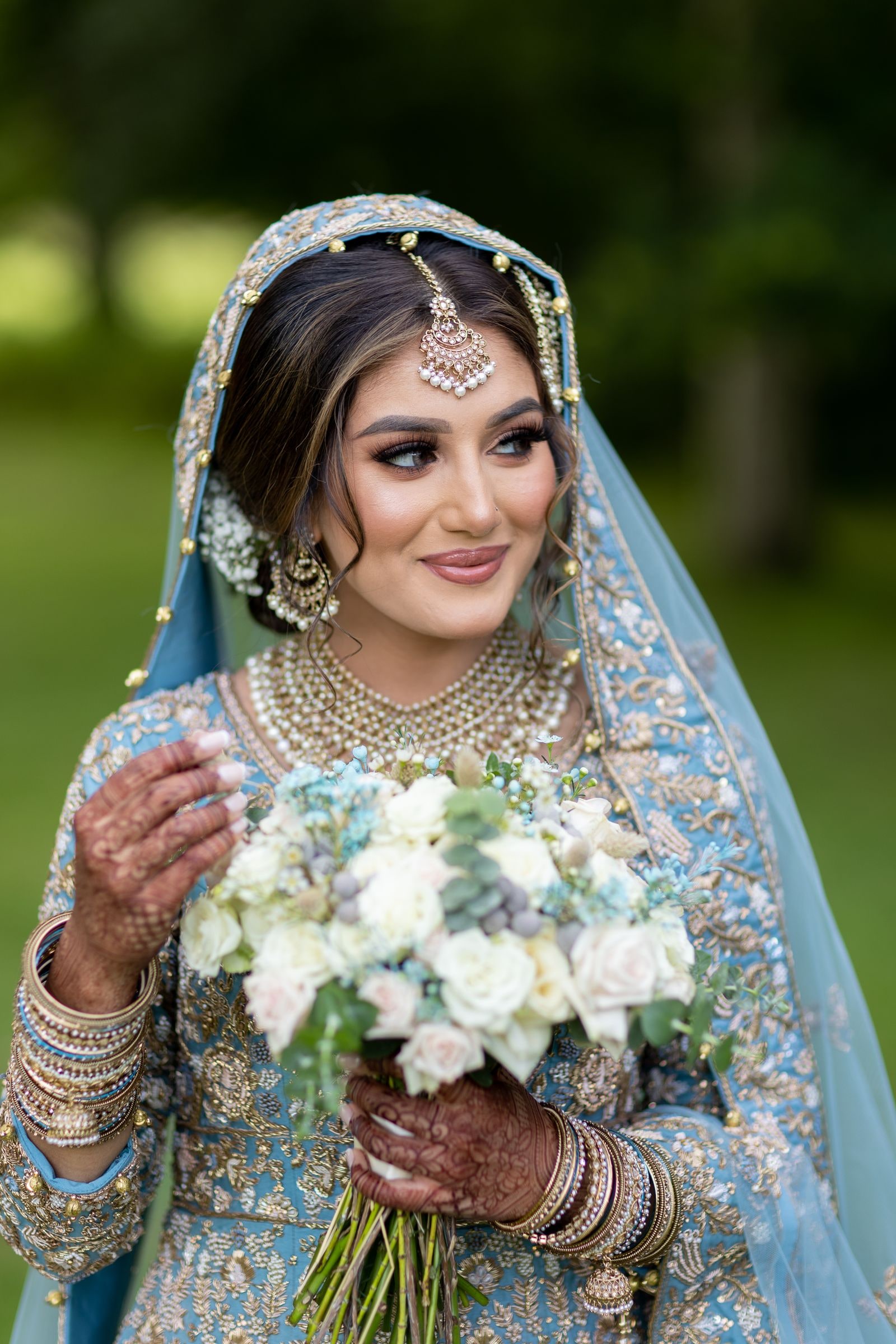 Bride holding a white and green bouquet, her hennaed hands stacked with gold bangles
