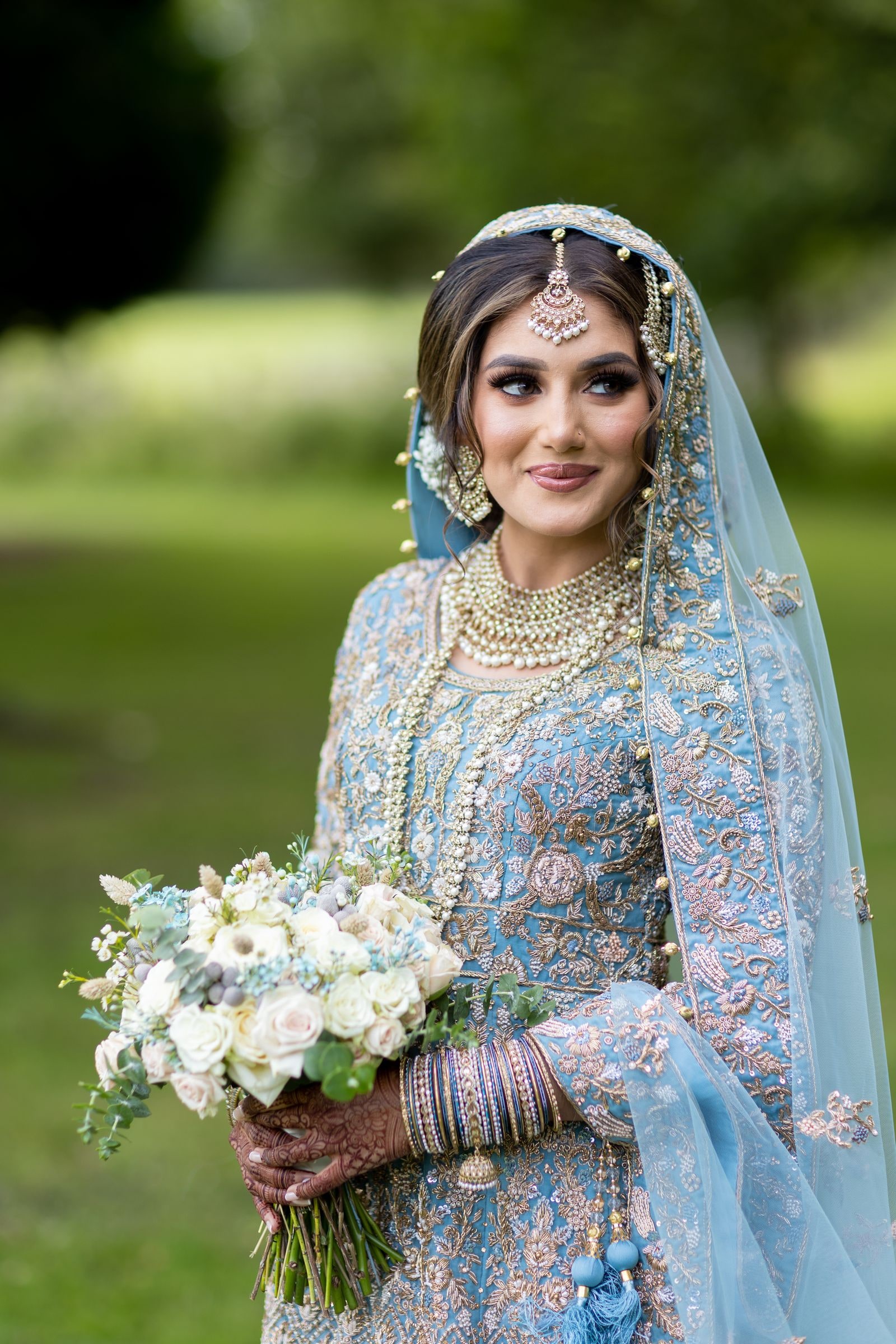Bride in profile with her bouquet, her dupatta pinned with pearls and gold