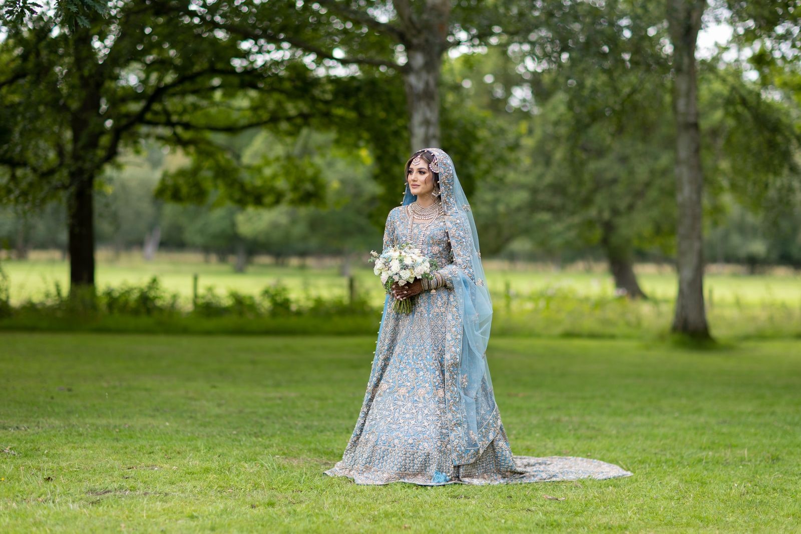 Bride alone in parkland with her bouquet, mature trees around her