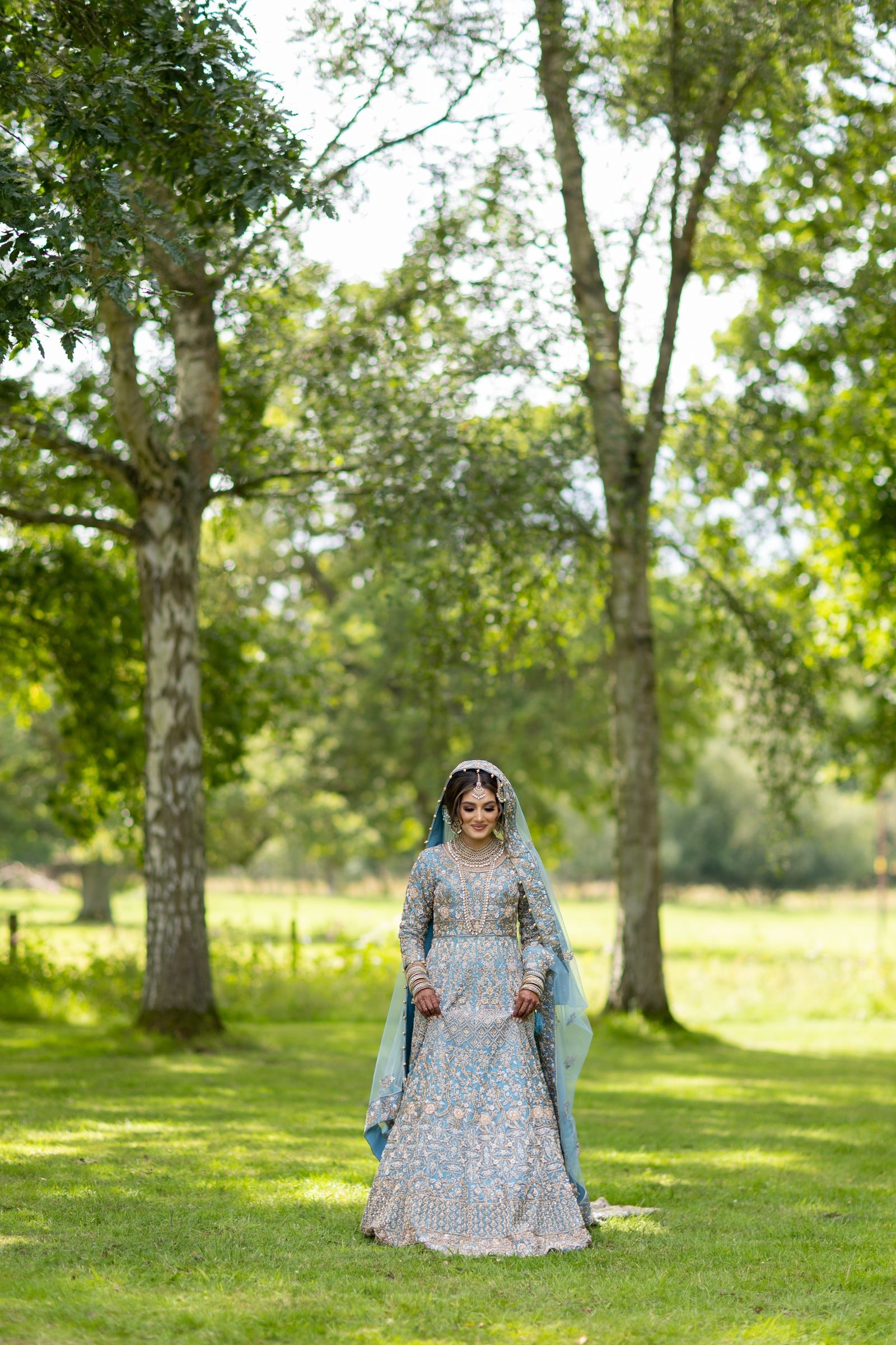 Bride walking towards the camera through dappled light under the trees