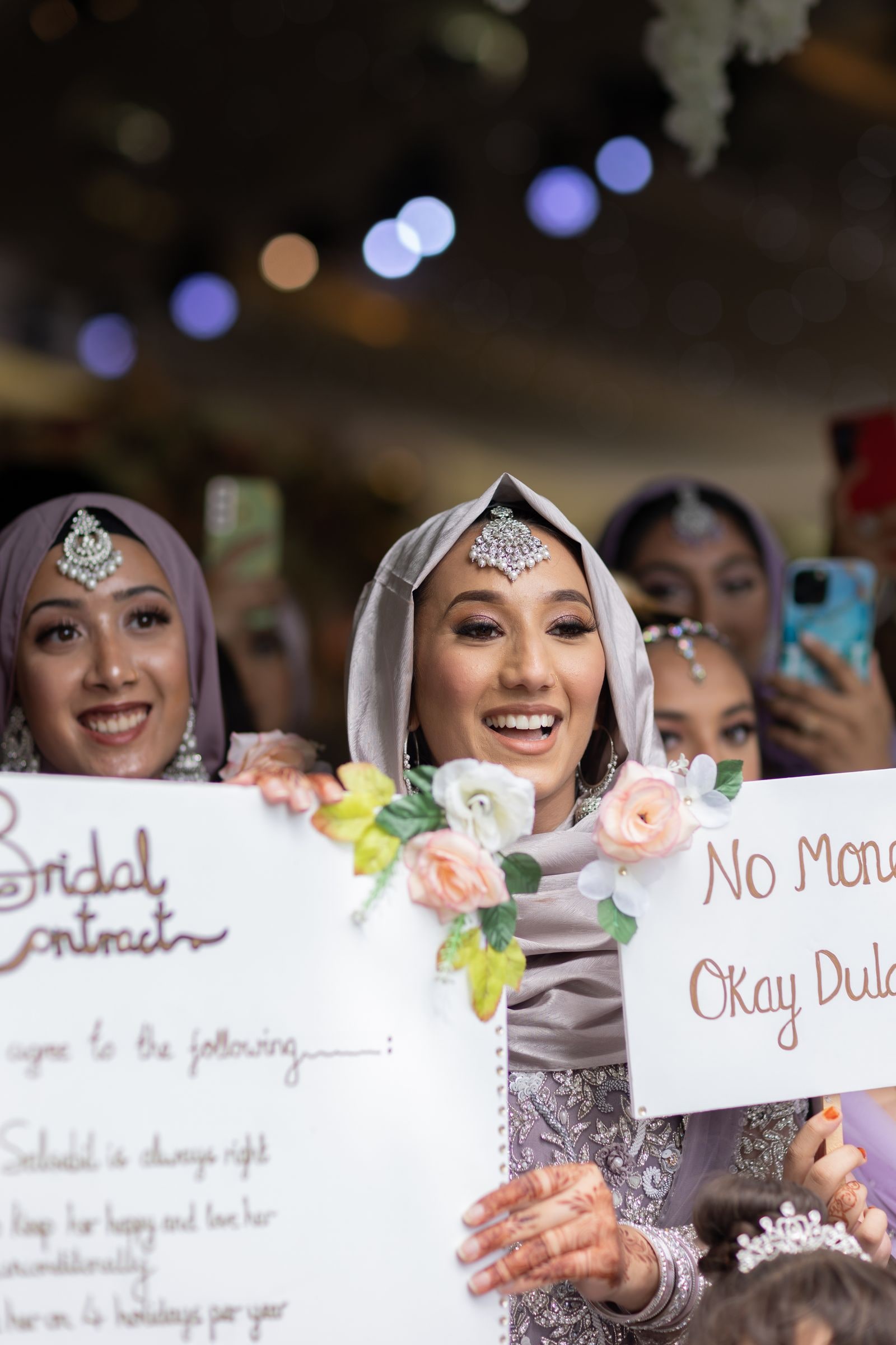 The bride's sisters holding up a handwritten bridal contract, laughing