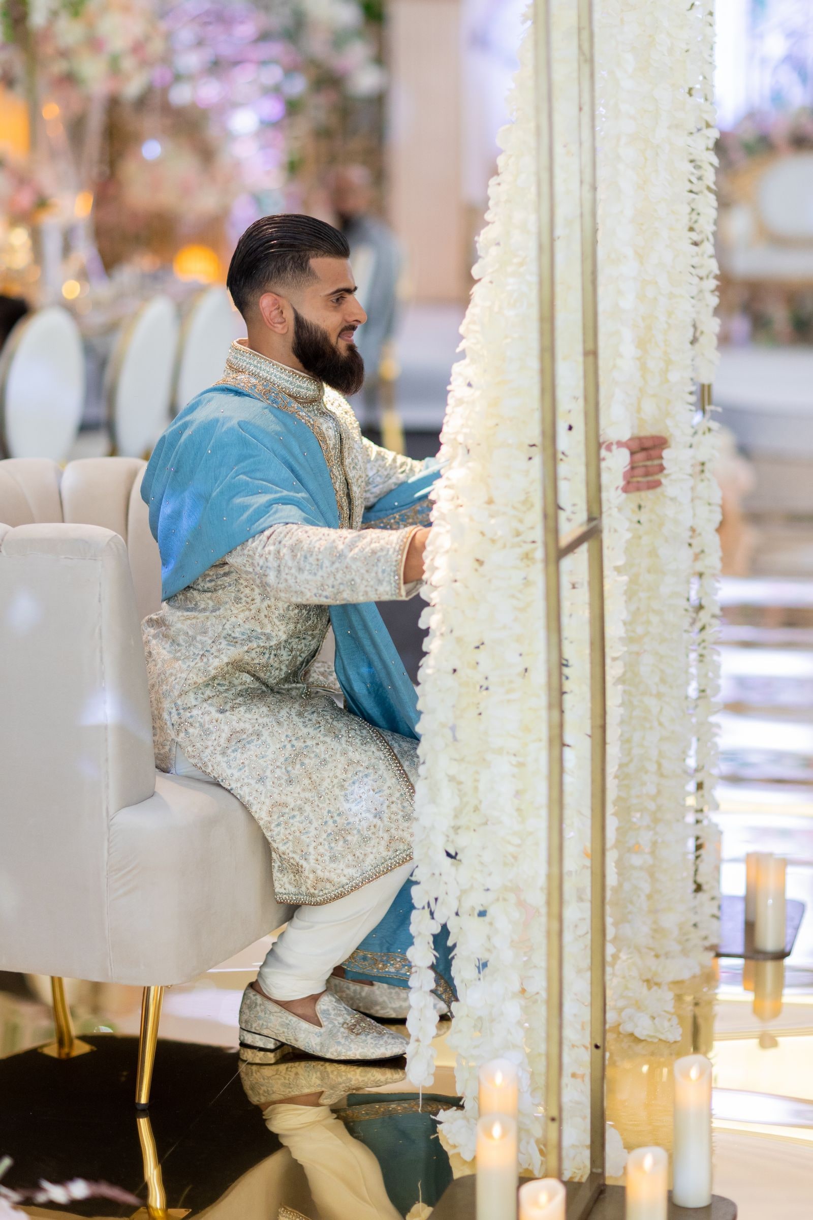 Groom seated behind a curtain of white flowers before the ceremony