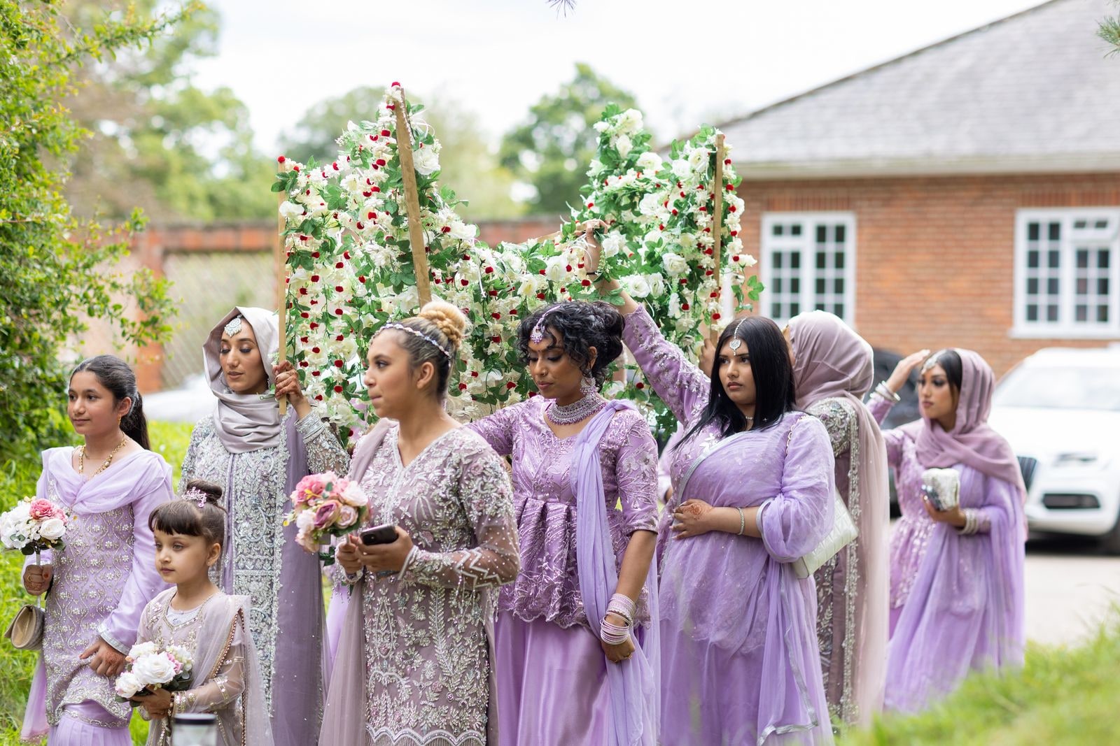 The bride's party in lilac carrying a flowered canopy across the grounds