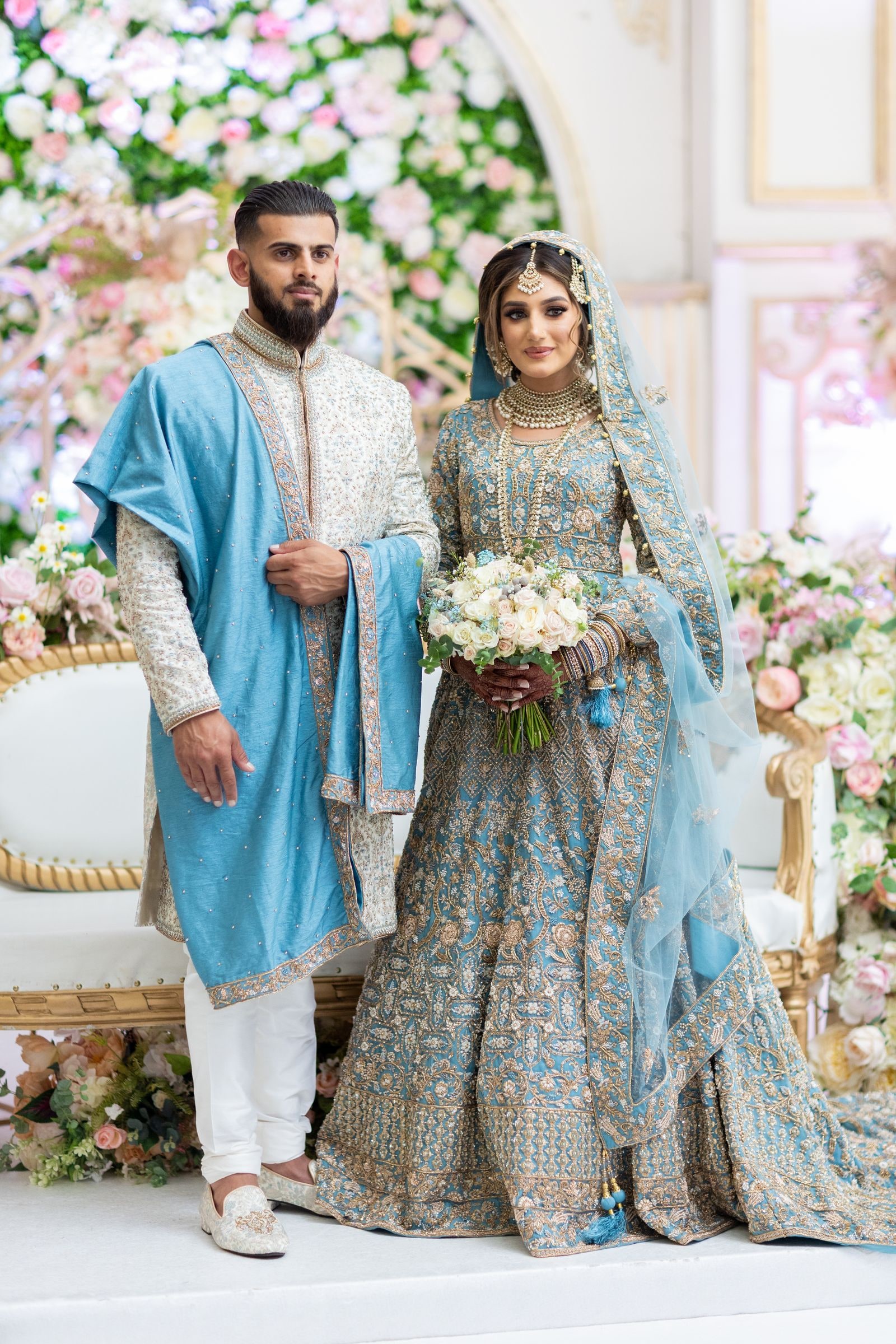Bride and groom standing together on the flowered stage, she holding a white bouquet