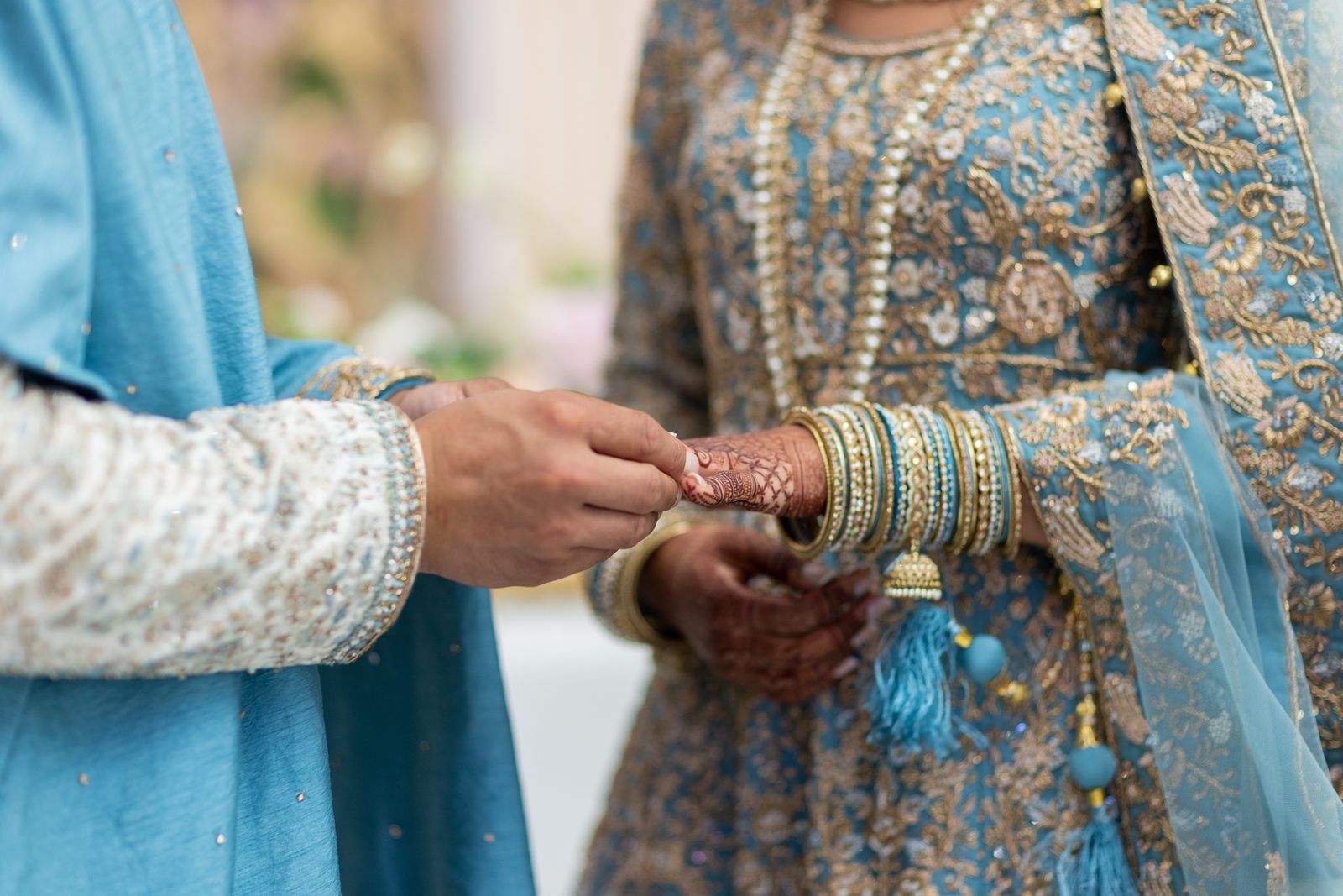 Close view of the groom putting a ring on his bride's hennaed hand, her bangles stacked to the wrist