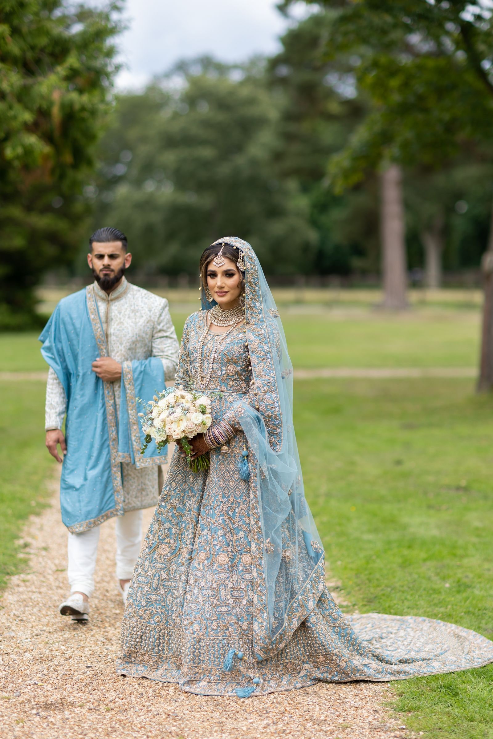 Bride and groom walking arm in arm along the path, her train sweeping behind