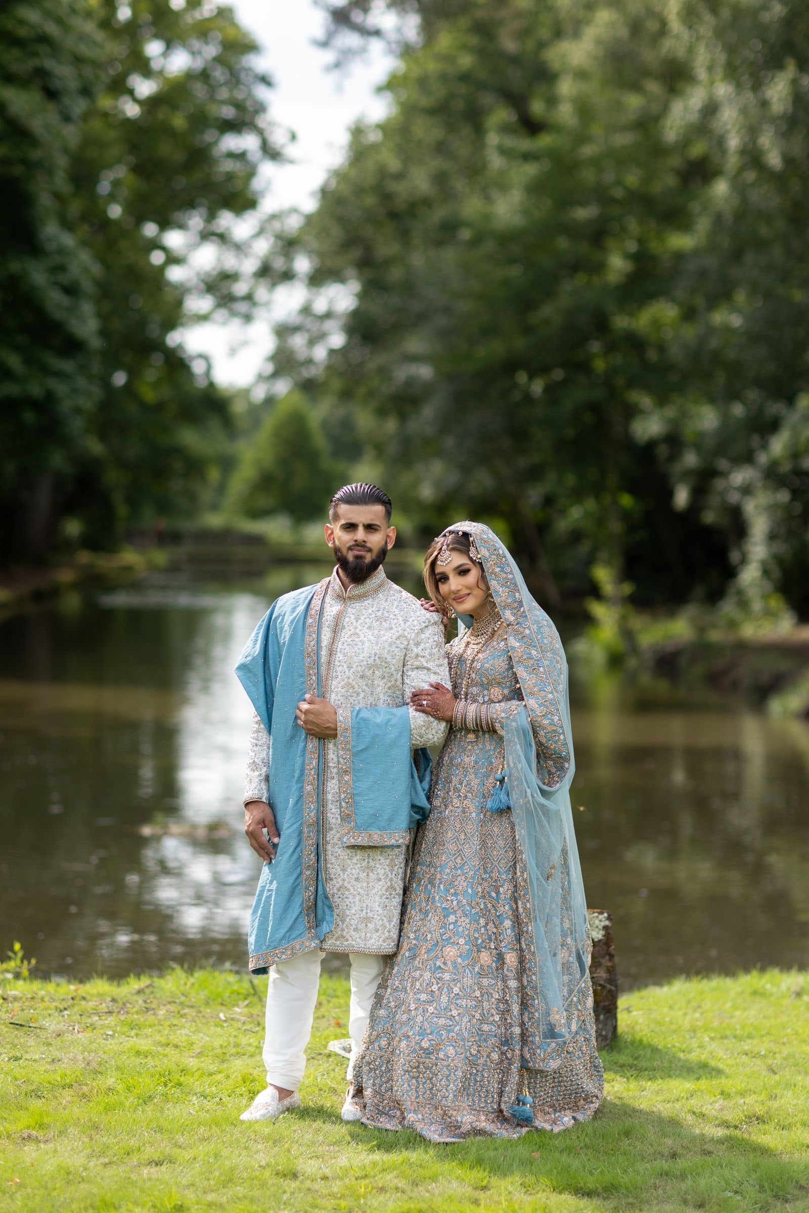 Bride and groom standing arm in arm beside the lake, trees closing in behind them