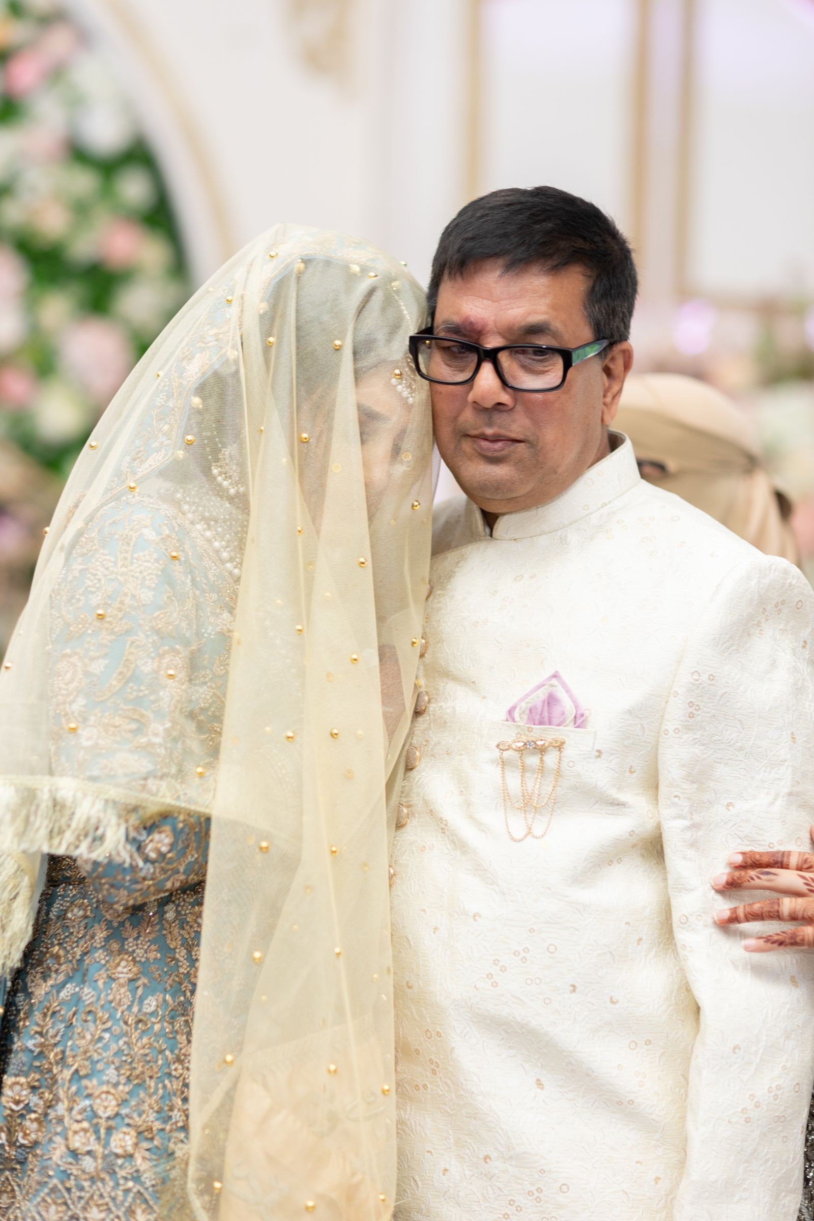 The bride's father in an ivory sherwani walking her in beneath her veil