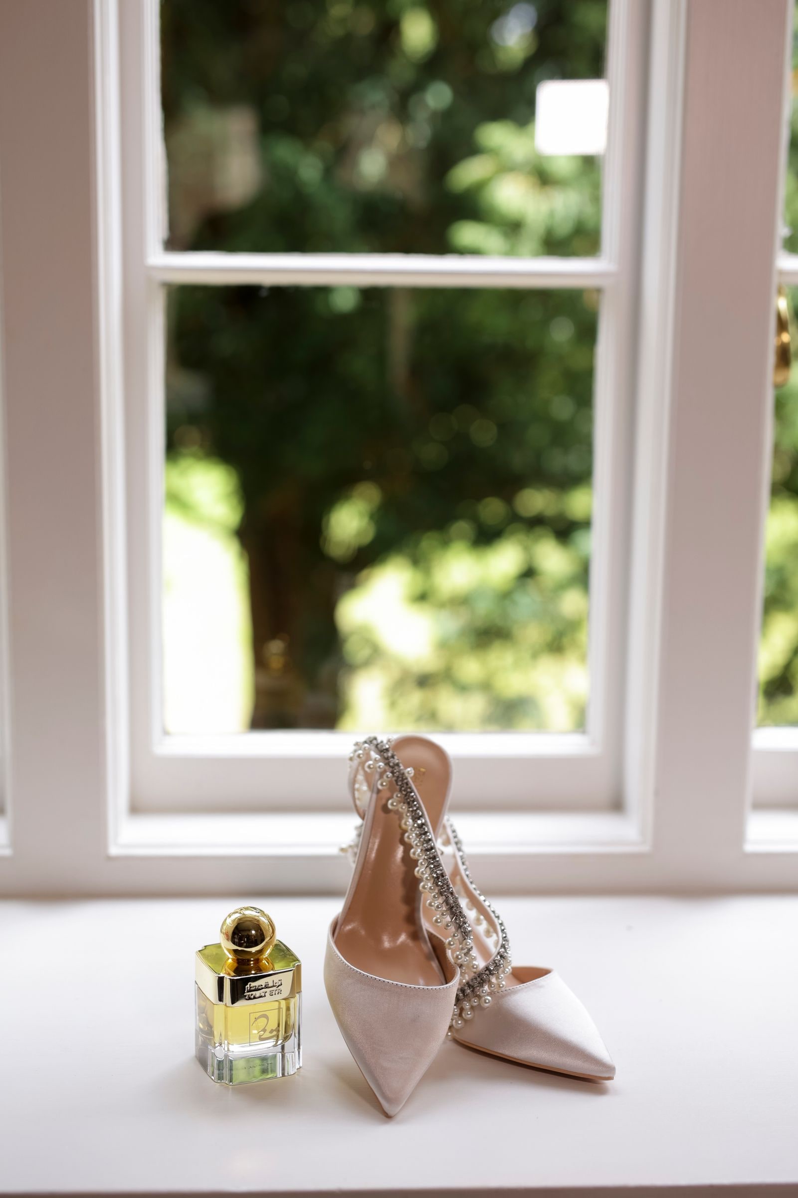 The bride's pearl-strapped shoes and perfume bottle on a windowsill
