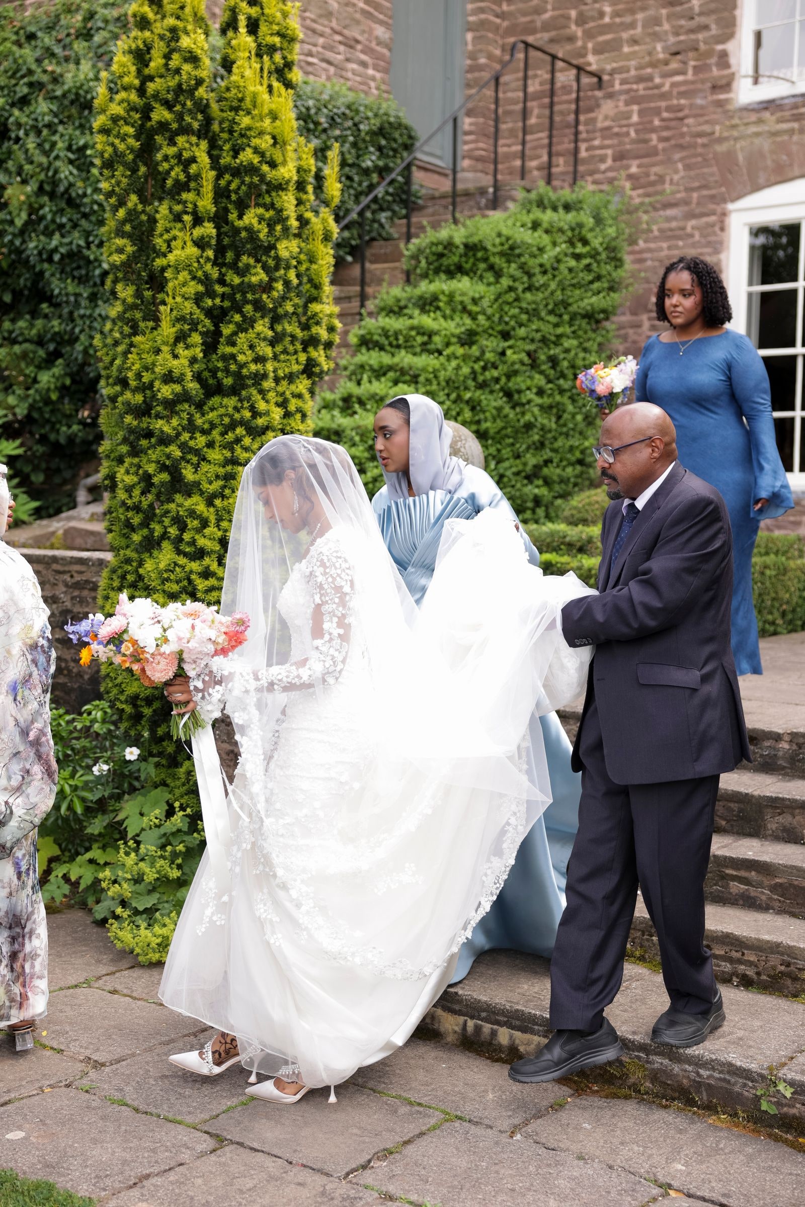 The bride's father helping her down the steps, her veil carried behind