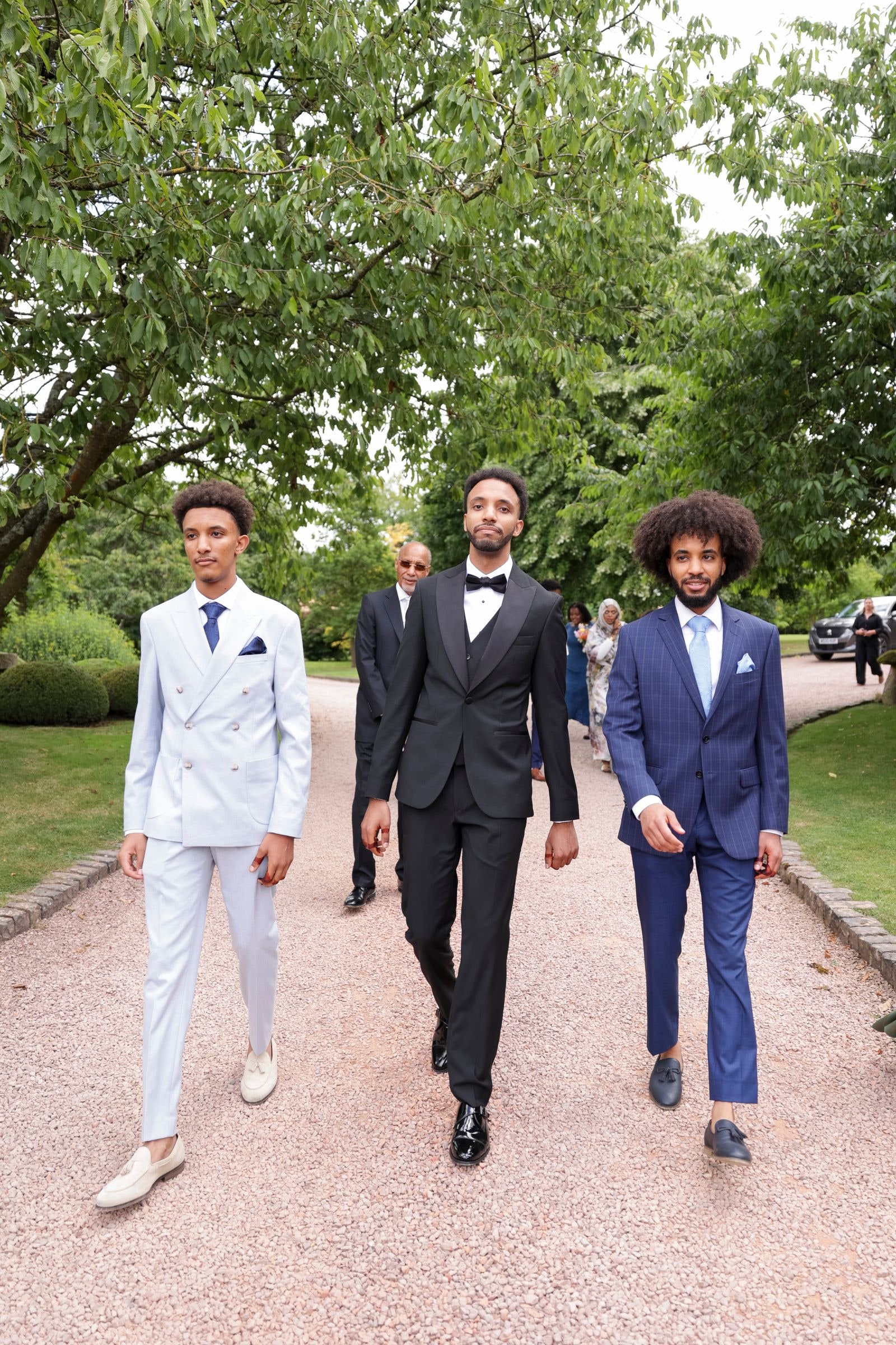 Groom in a black tuxedo walking the path with his two groomsmen