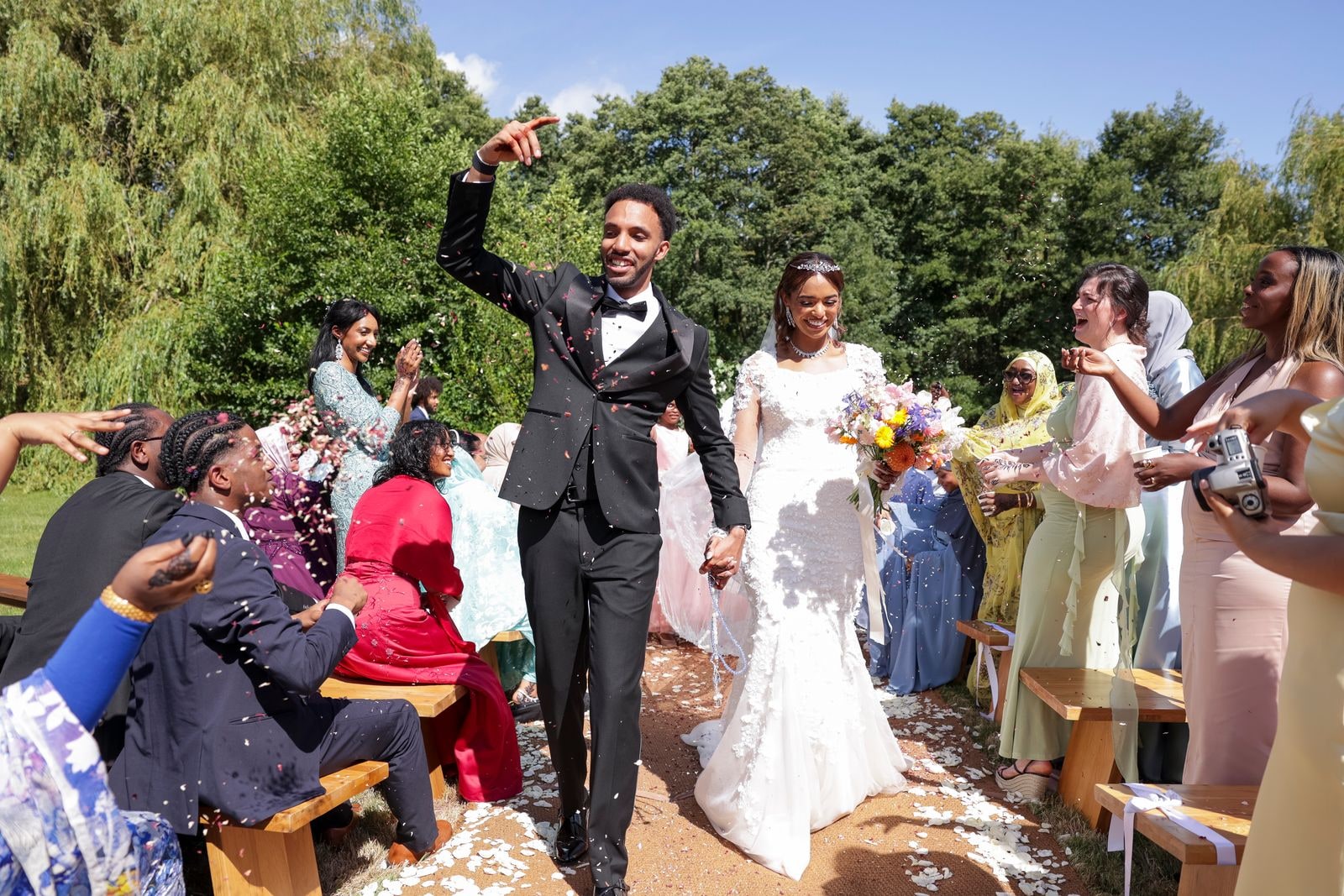 Bride and groom walking back down the aisle, his fist raised, confetti falling