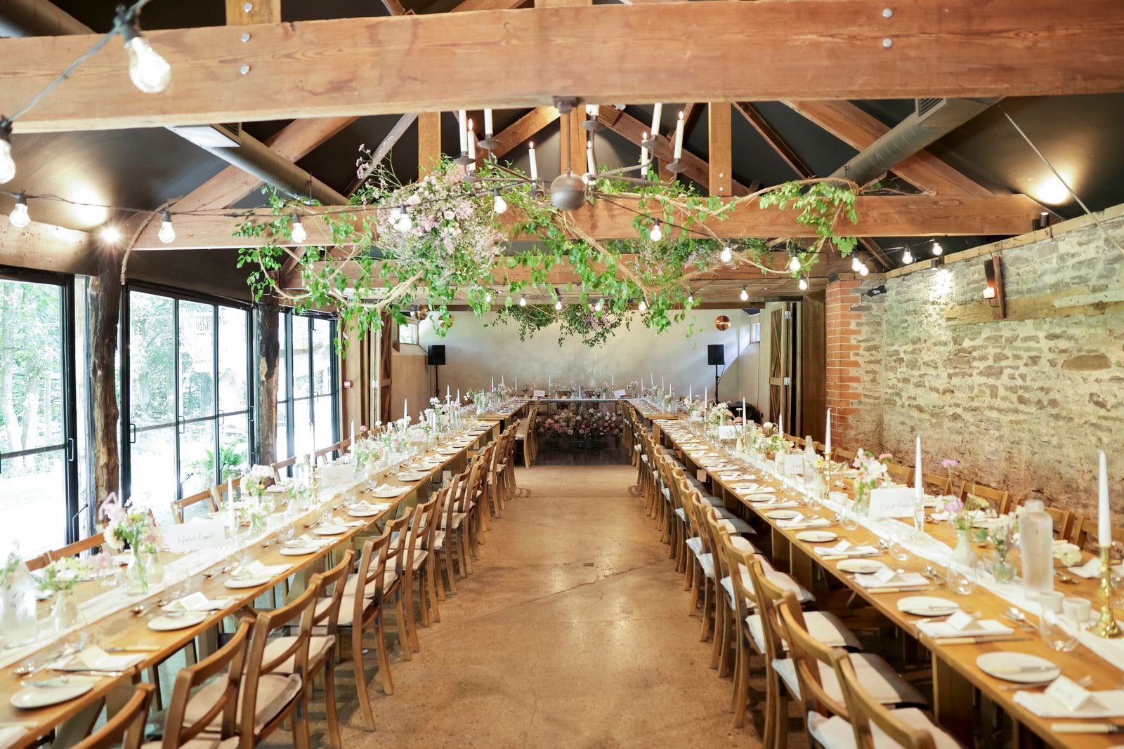 The barn laid for dinner, long tables under a hanging garland of greenery