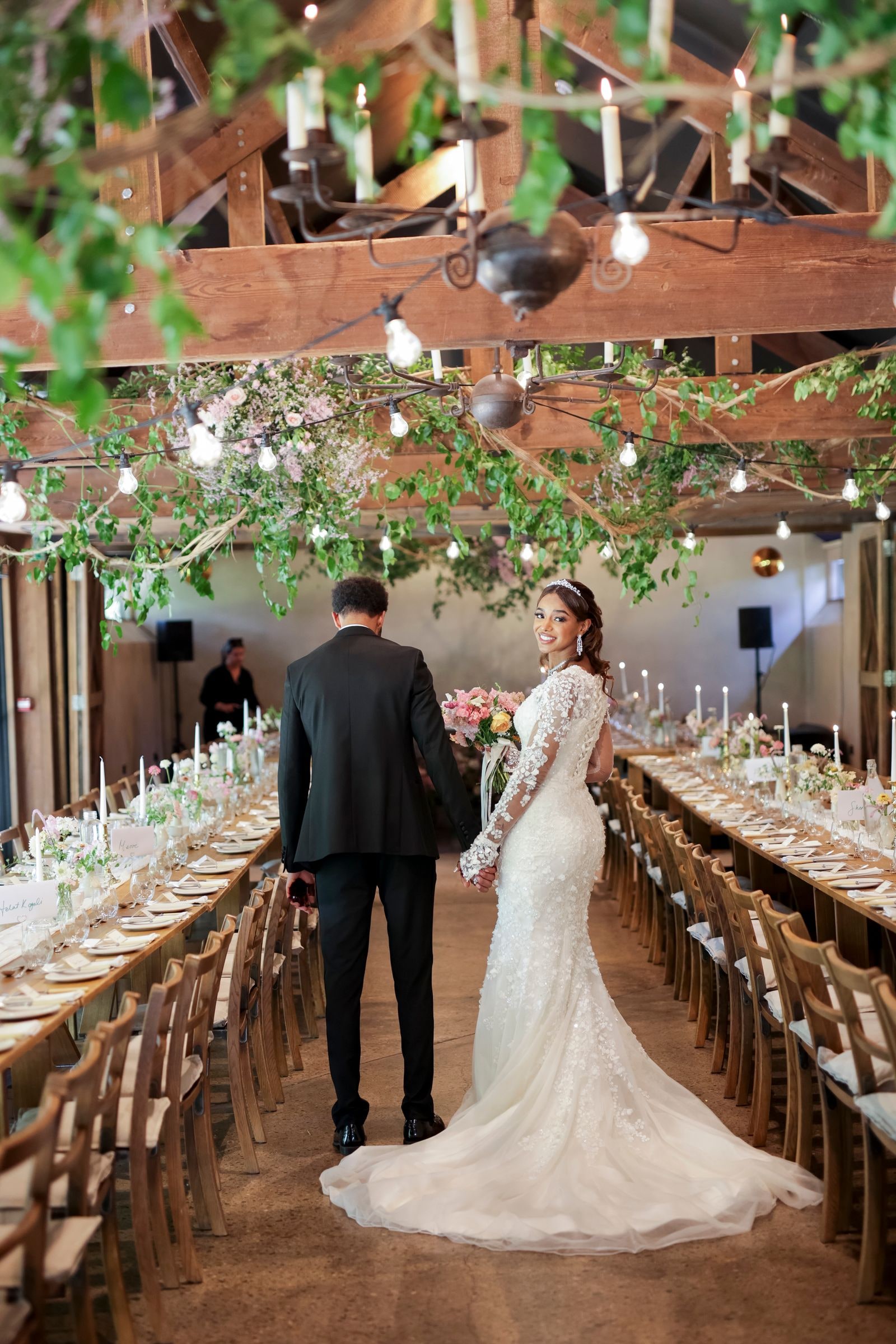 Couple walking away up the barn between the tables, her train behind her