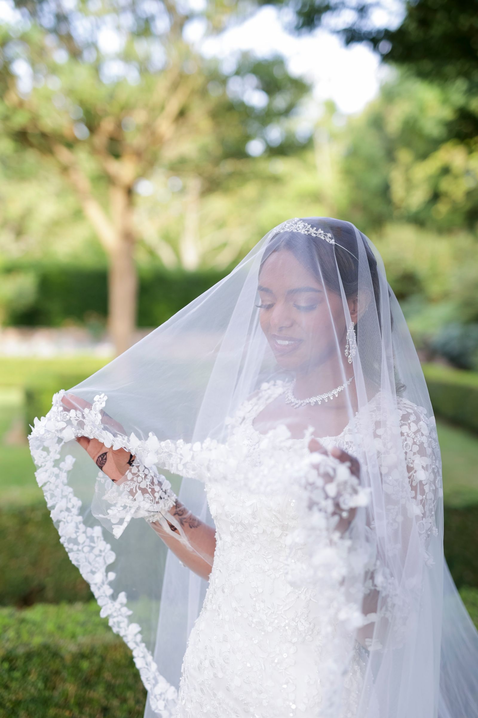 Bride holding her lace veil out to one side in the garden