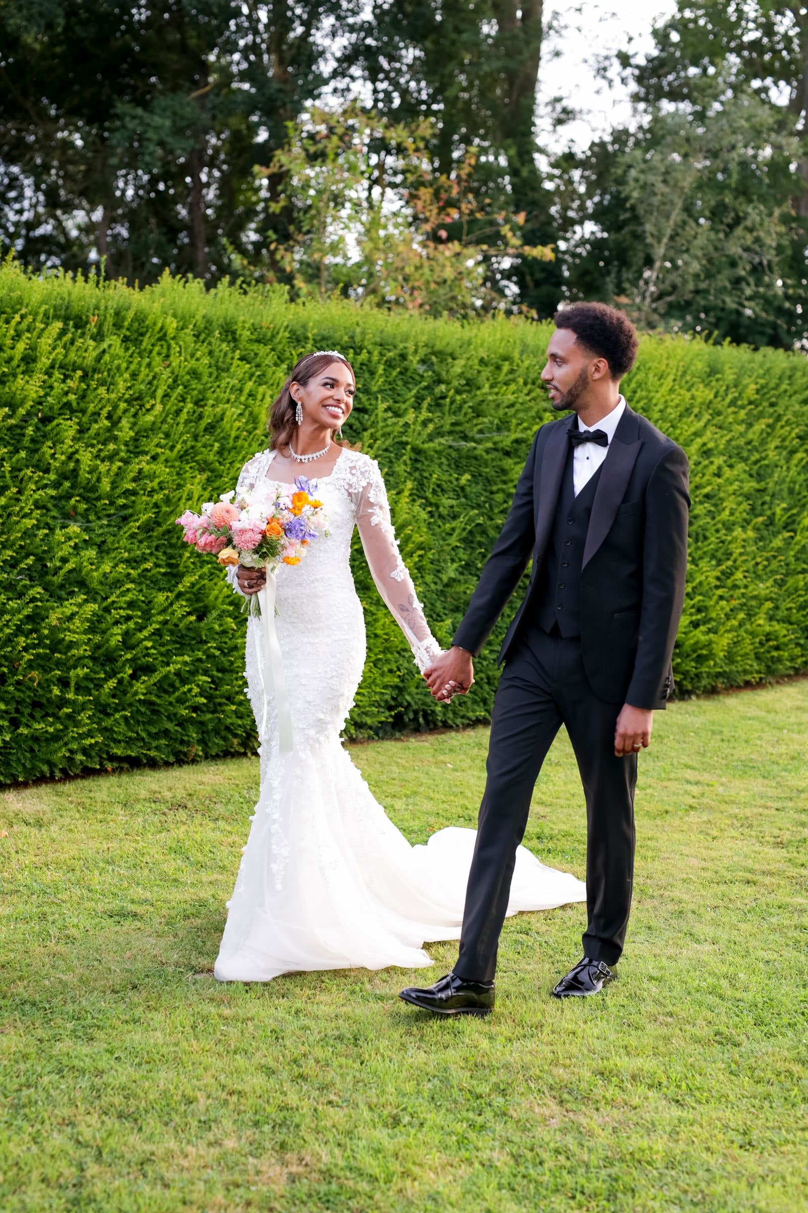 Couple walking the grass hand in hand, the bride with her wildflower bouquet