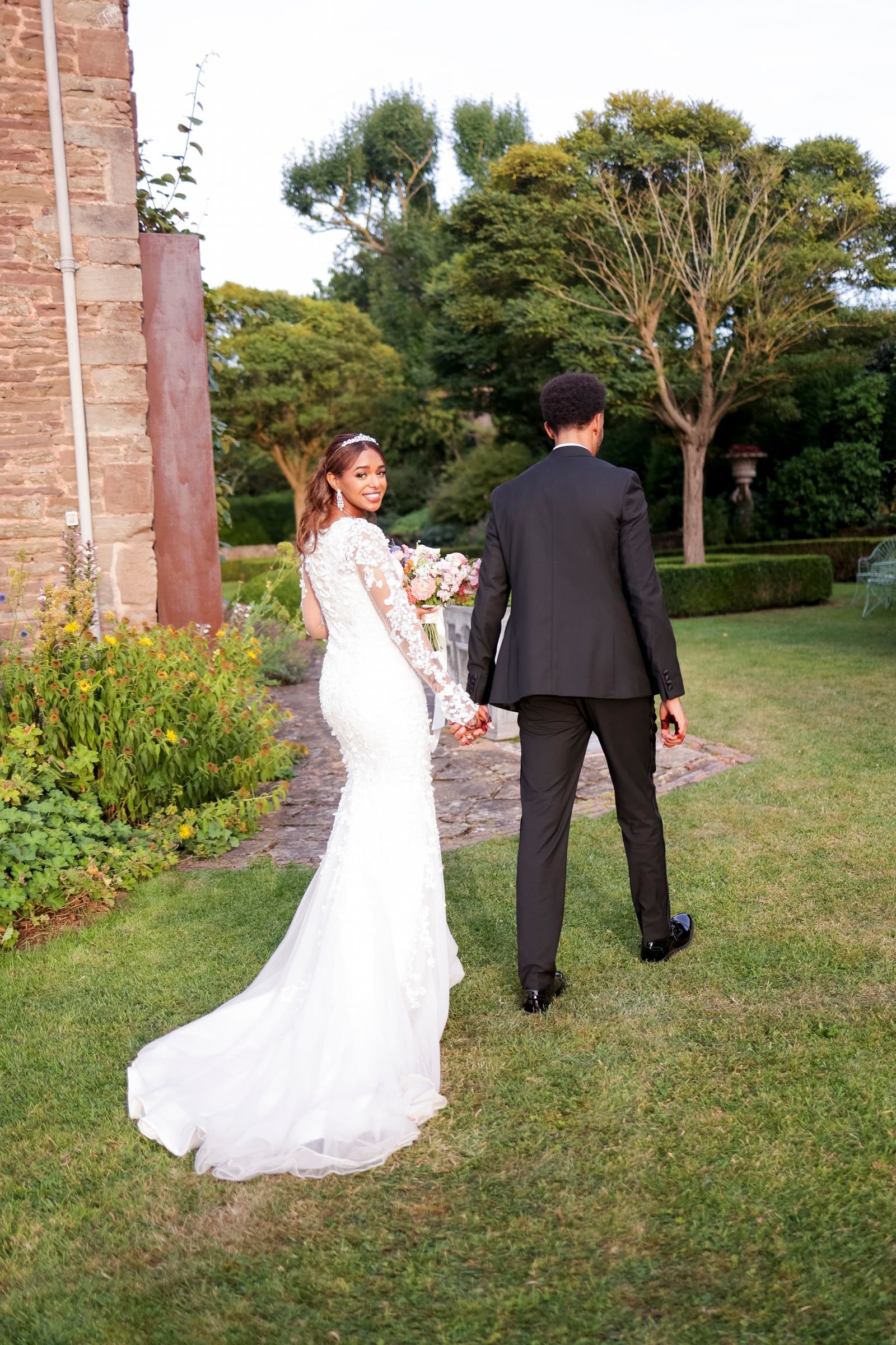 Bride and groom walking away across the lawn, her train trailing behind