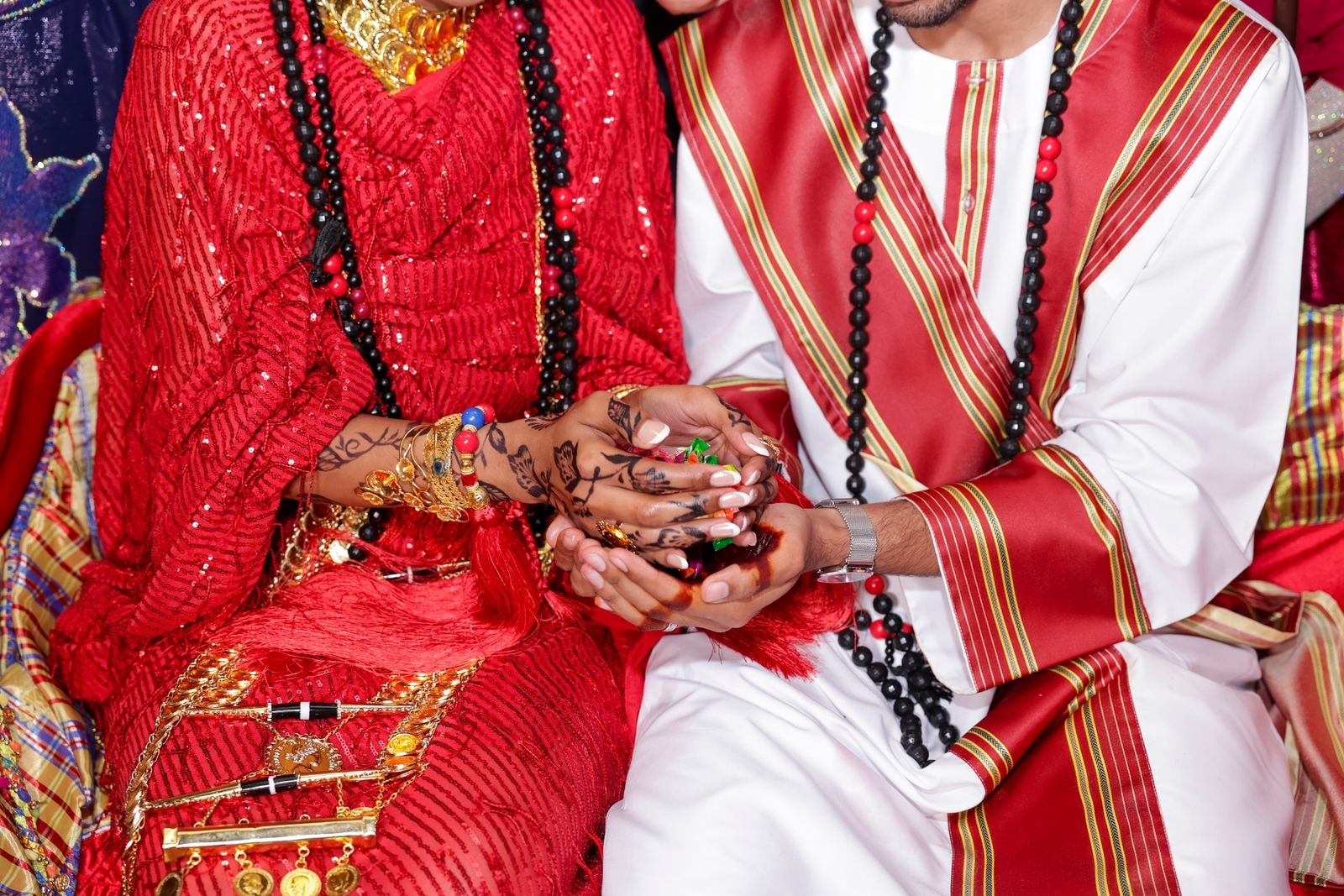 Close view of the couple's joined hands in red and white embroidered dress, gold at her wrists