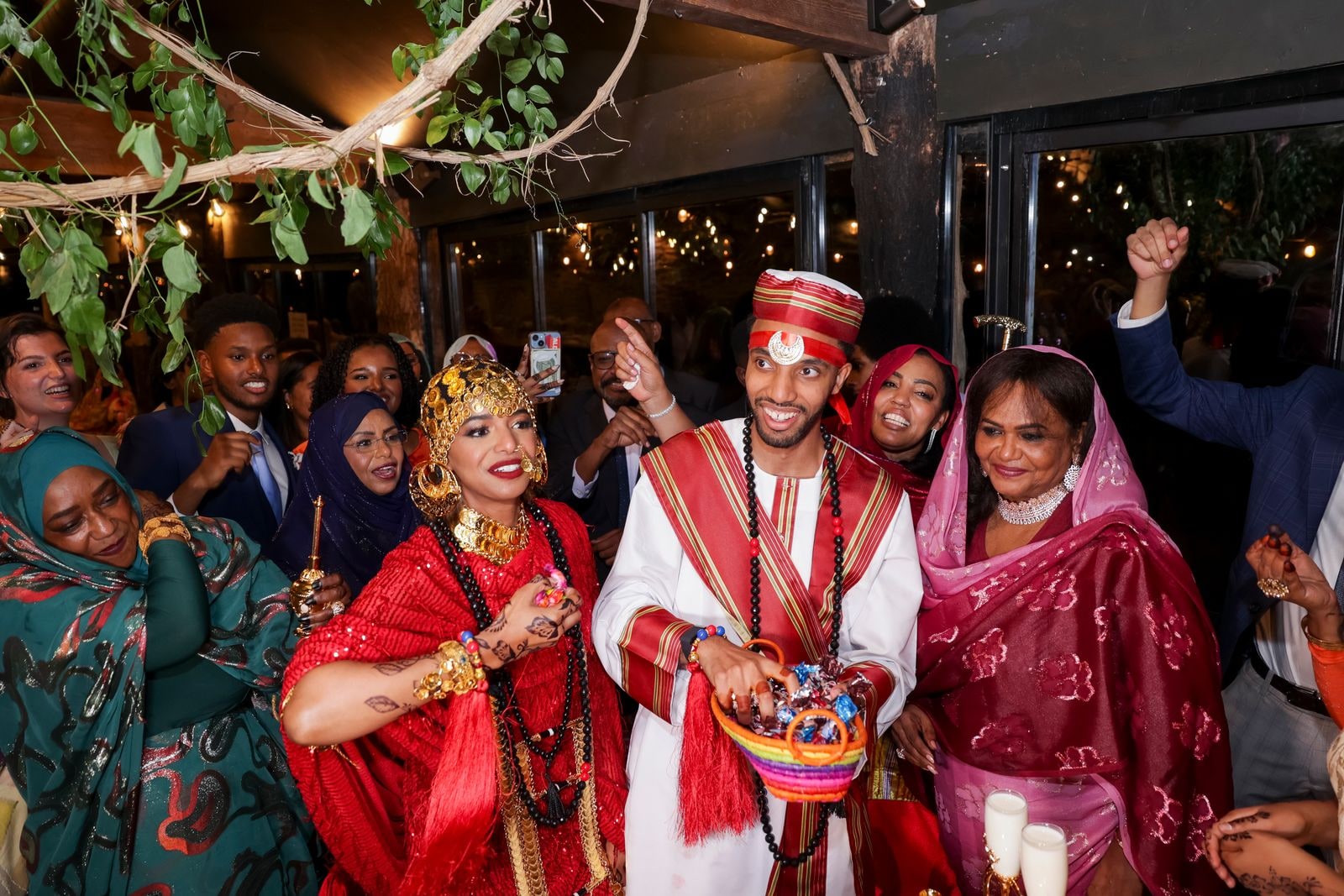 Bride and groom in red and white among the guests, she carrying a woven basket