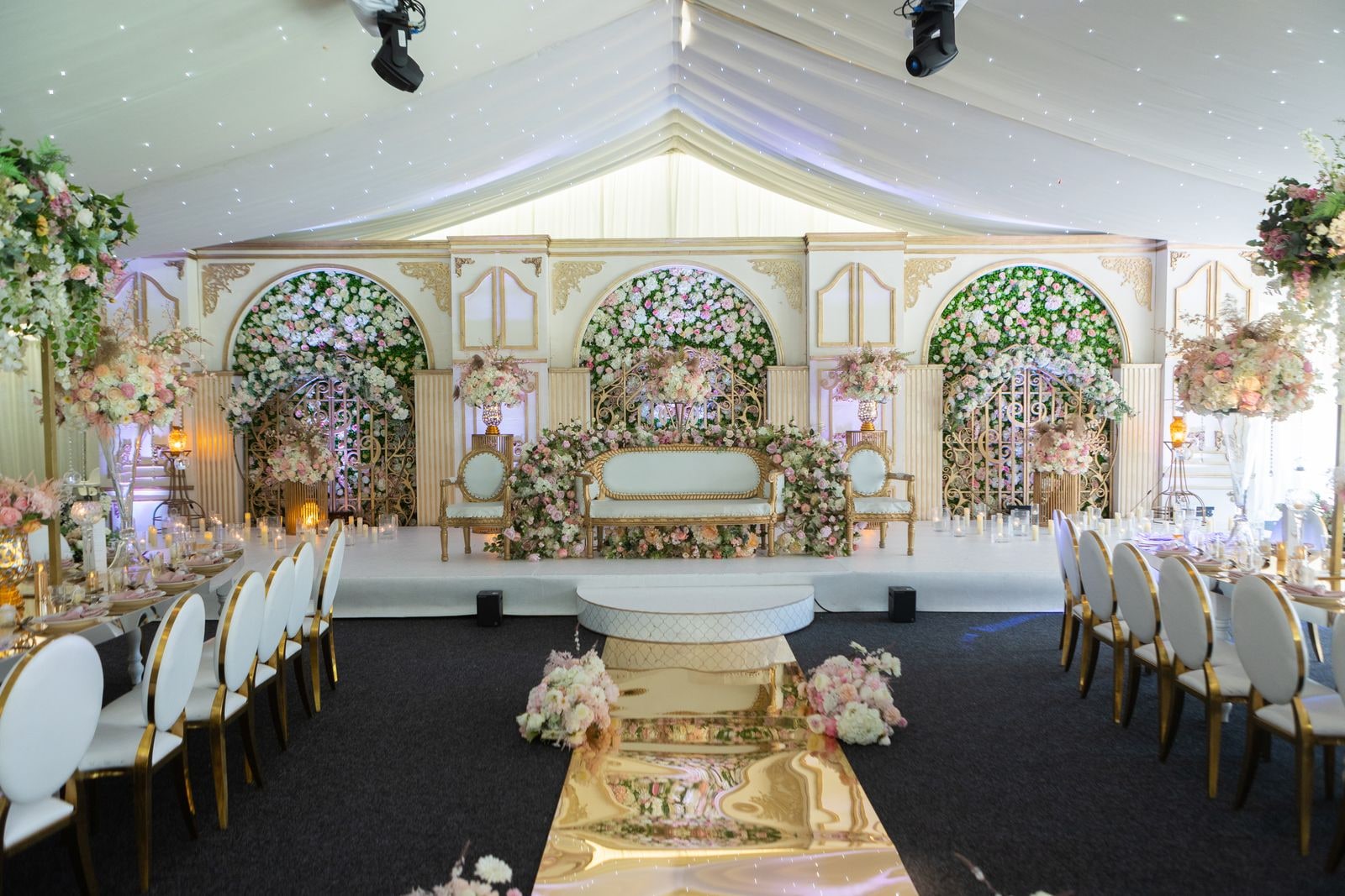 The empty ceremony room before guests arrive, flowered stage and gold aisle