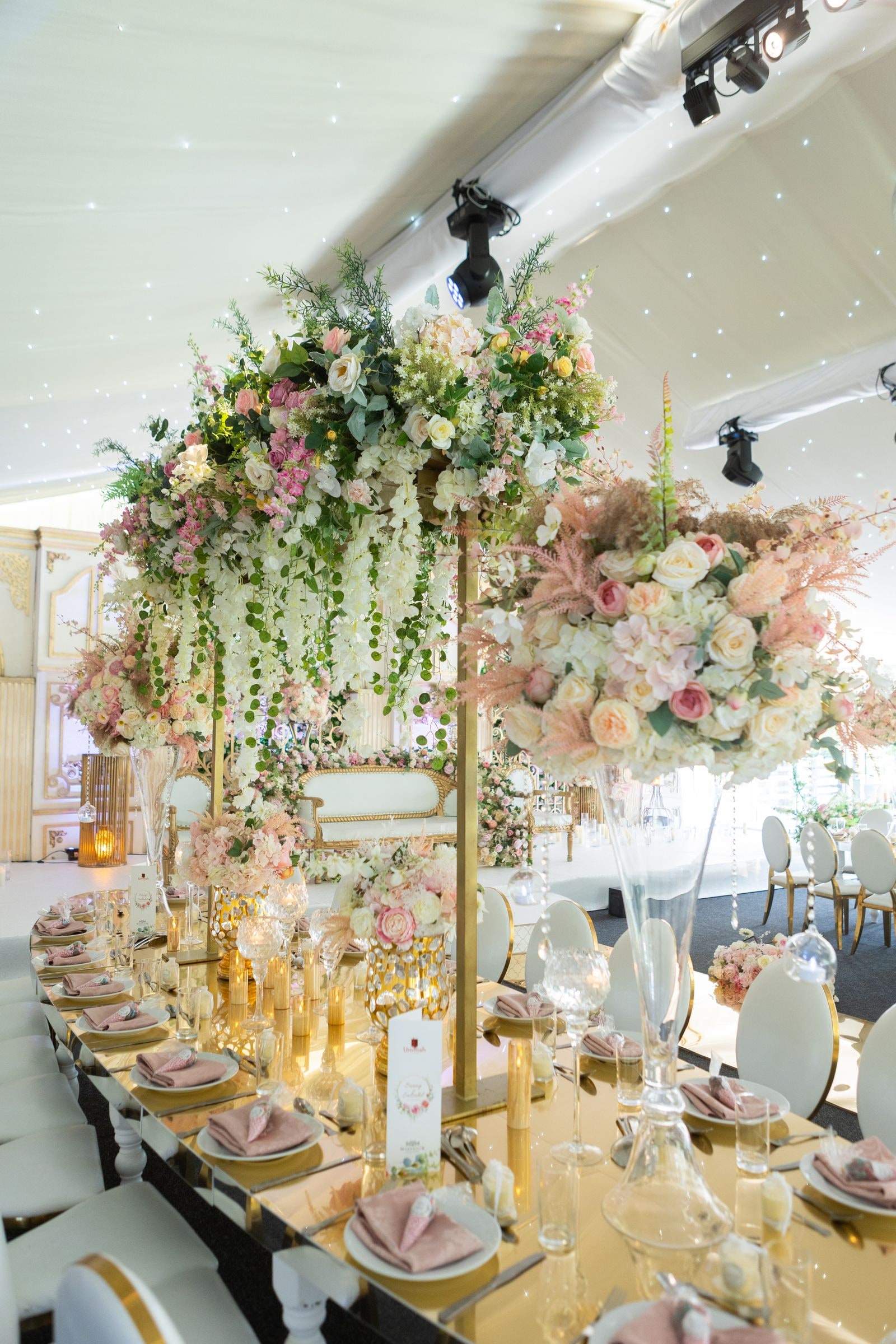 The long table laid with pink and gold, hanging flowers suspended above it