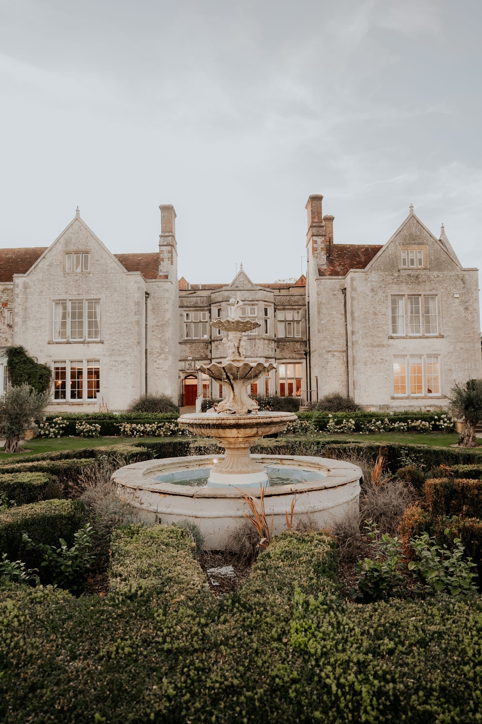 The stone house and its fountain seen across the formal garden at dusk