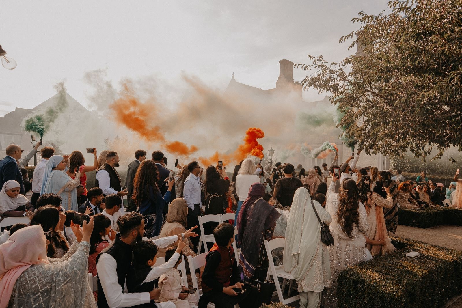 Guests seated in the garden as orange and green smoke drifts across them