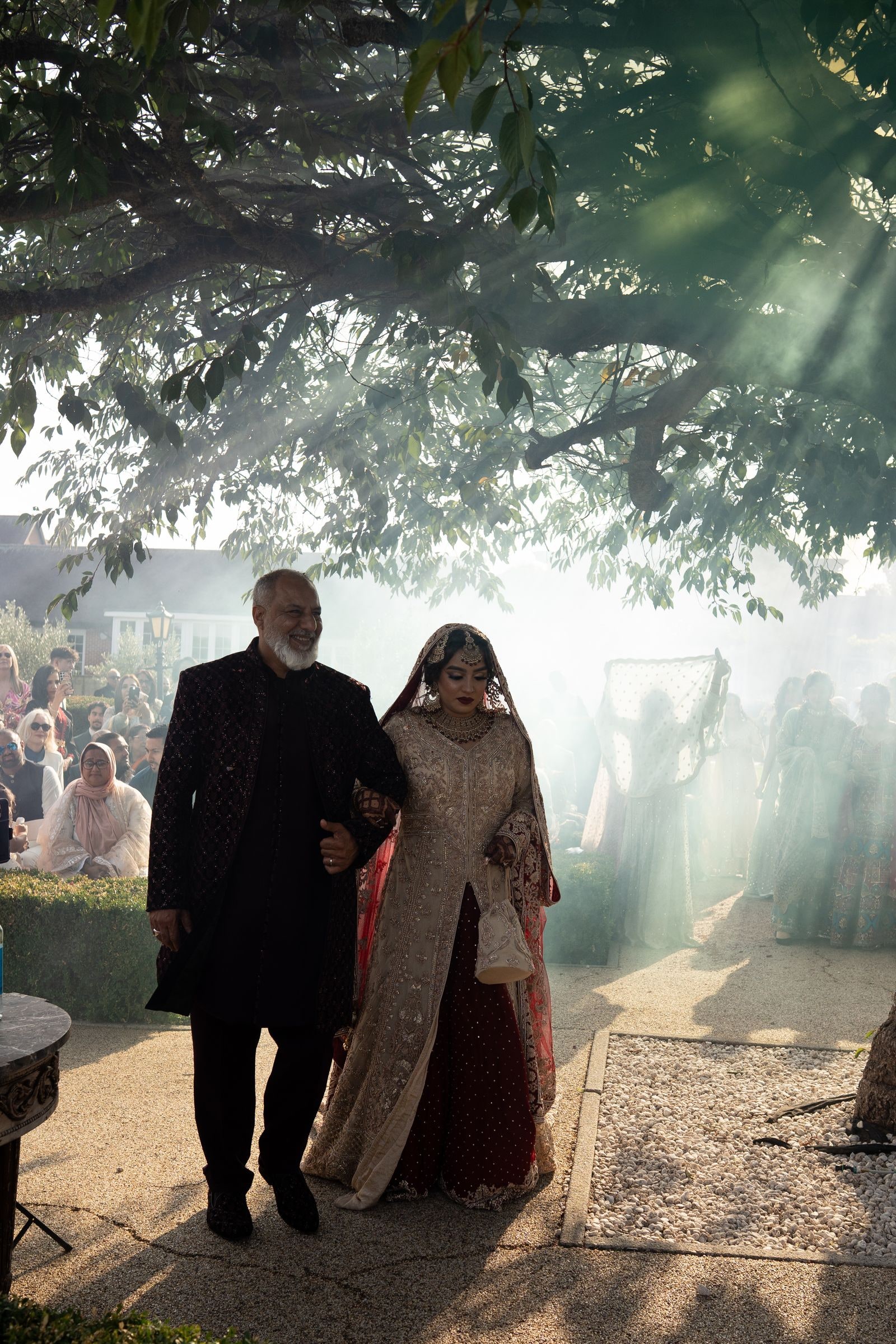 The bride's father walking her towards the ceremony through drifting smoke
