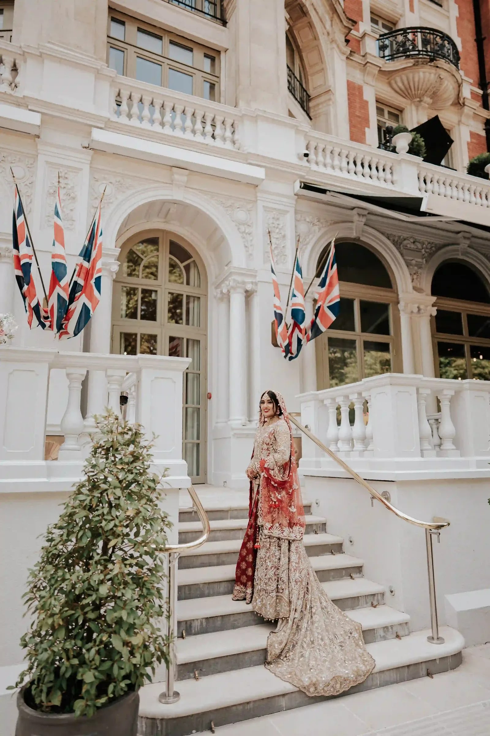 Bride on the hotel steps in gold and red, her train falling down the stone