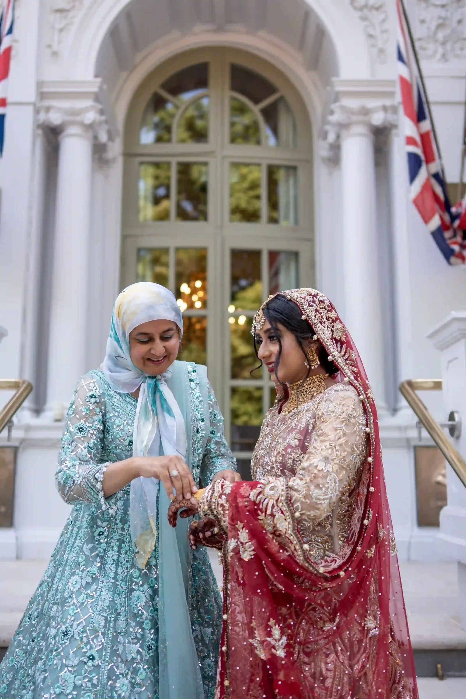Two women in pale blue and red talking on the hotel steps, hands joined