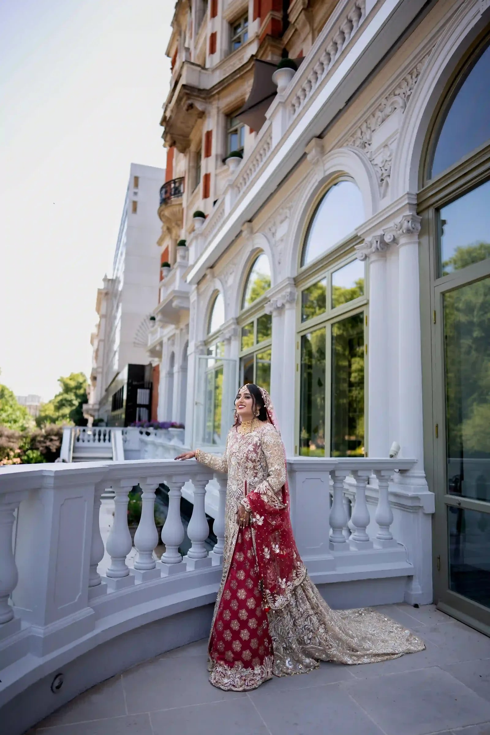 Bride on a balustraded terrace in a red and gold gown, her train spread behind her