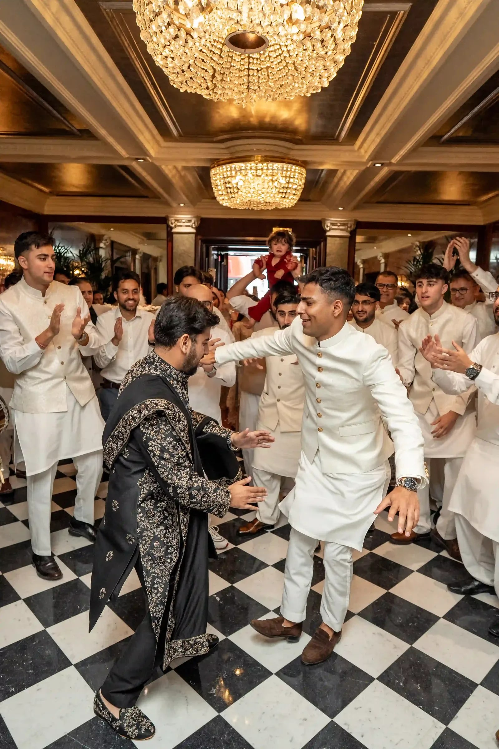 The groom dancing in across a chequered marble floor as friends applaud