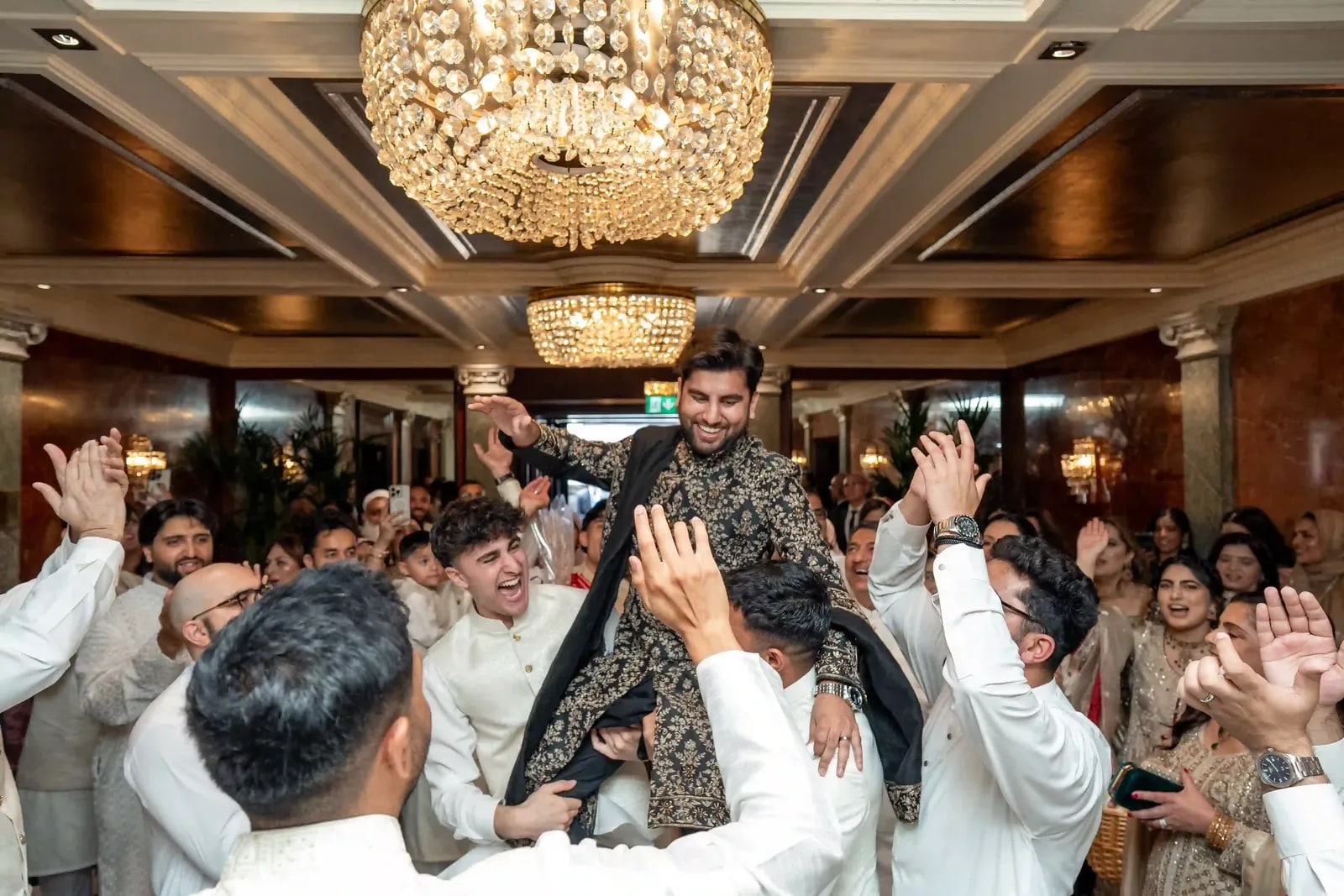Groom lifted above the crowd in the hotel lobby, hands raised all round him