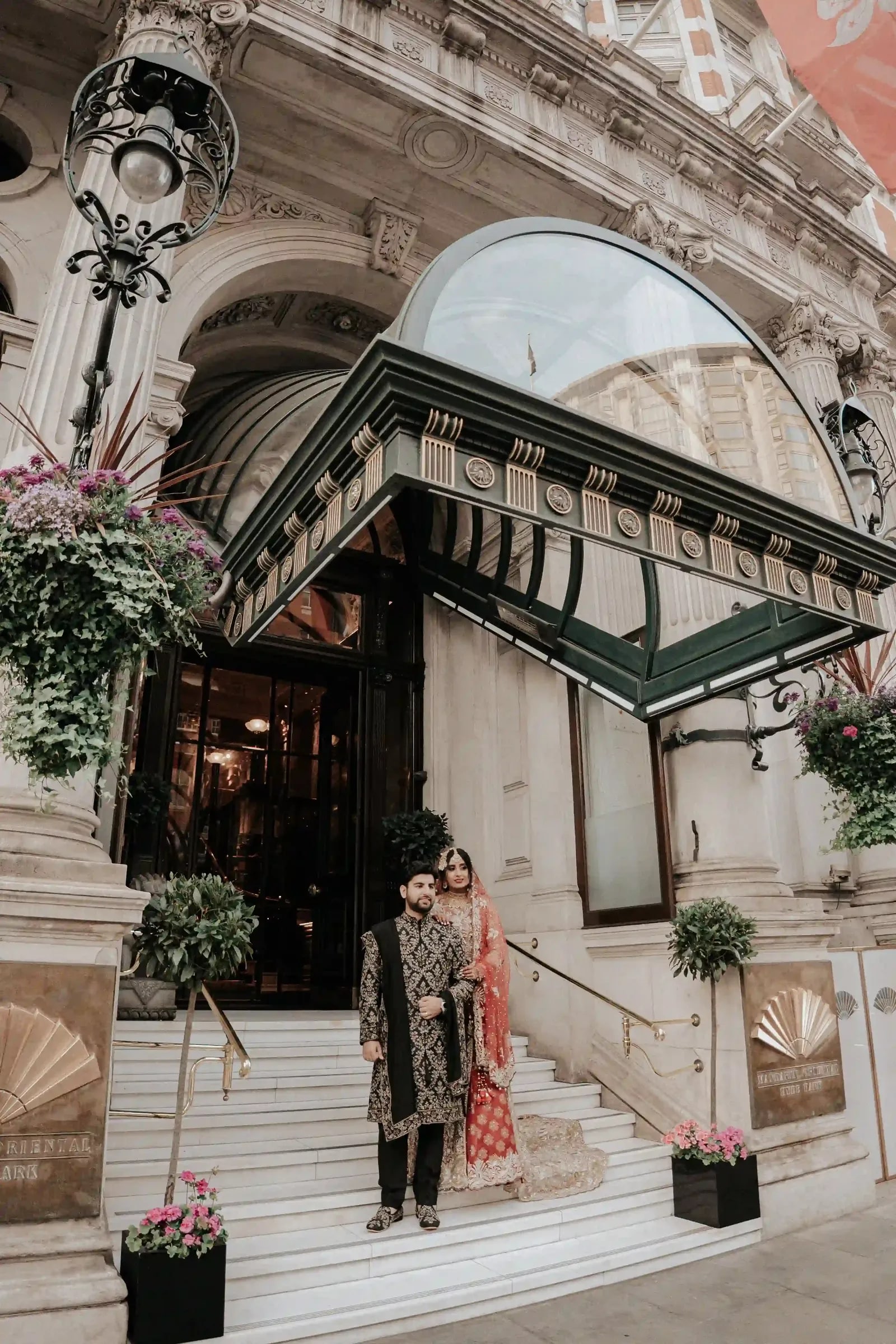 Bride and groom standing together under the green glass canopy of the hotel entrance