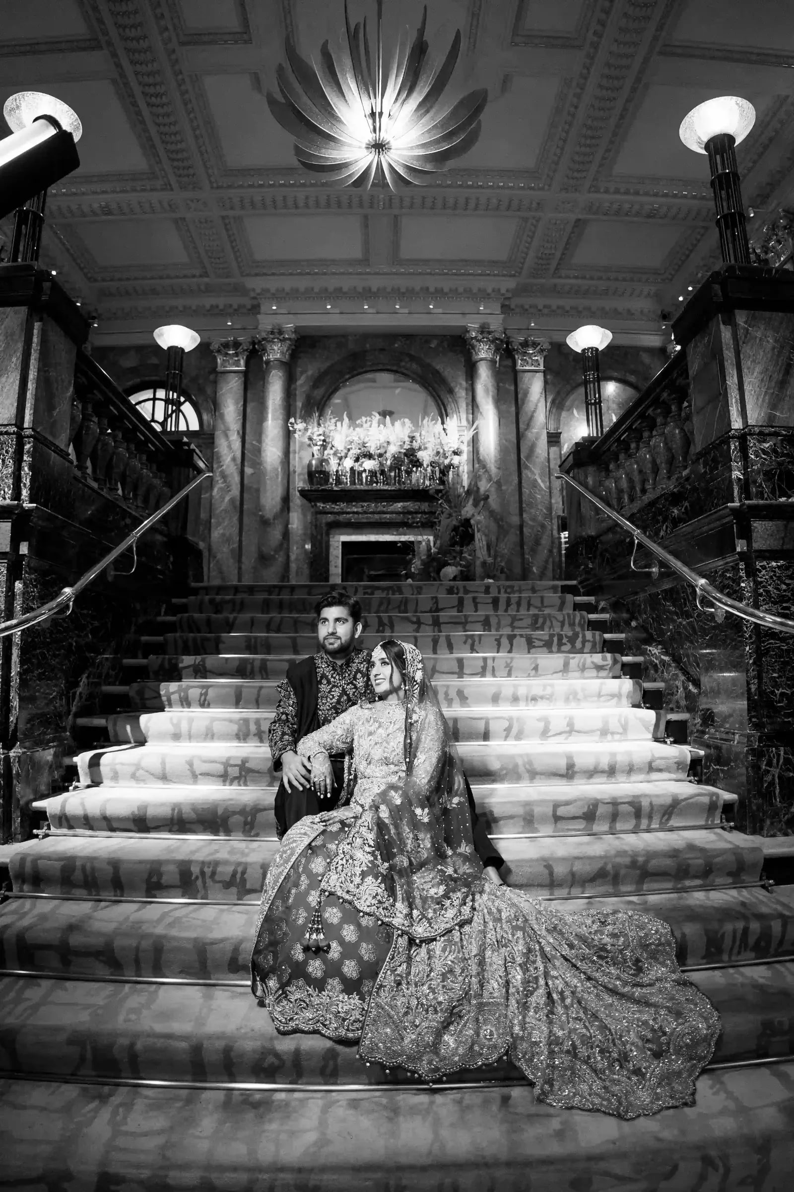 Couple seated on a grand marble staircase, her train spilling down the steps, in black and white