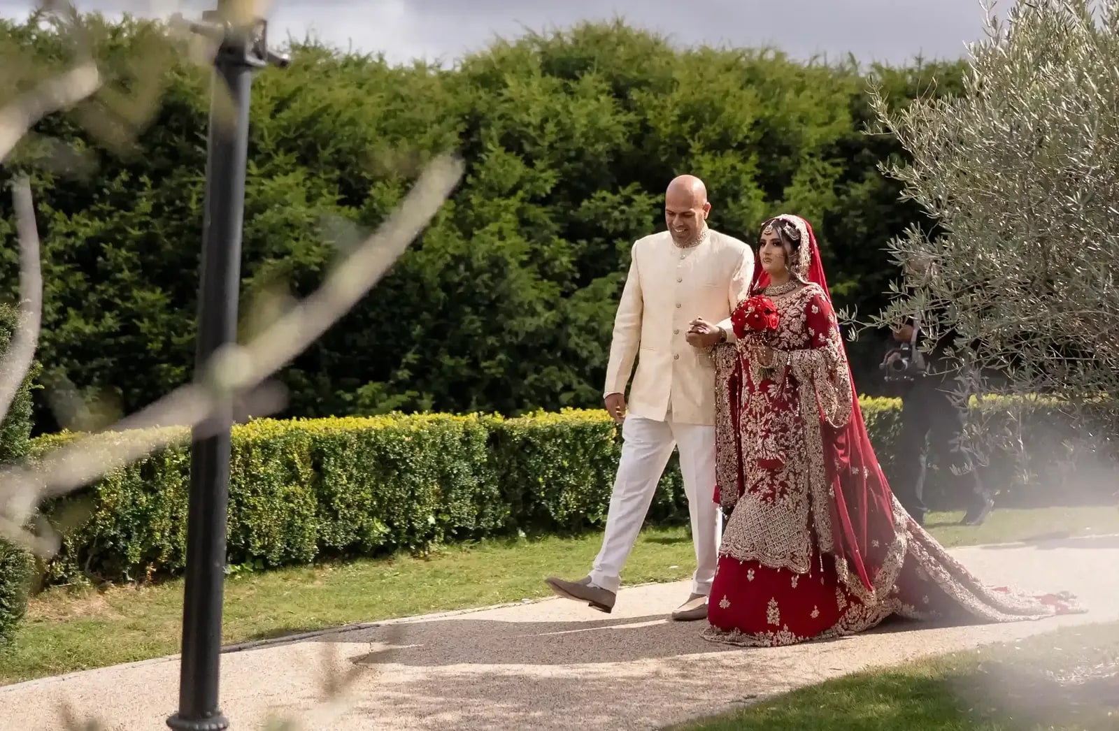 Bride and her father on the path past the lamp post, framed by olive branches