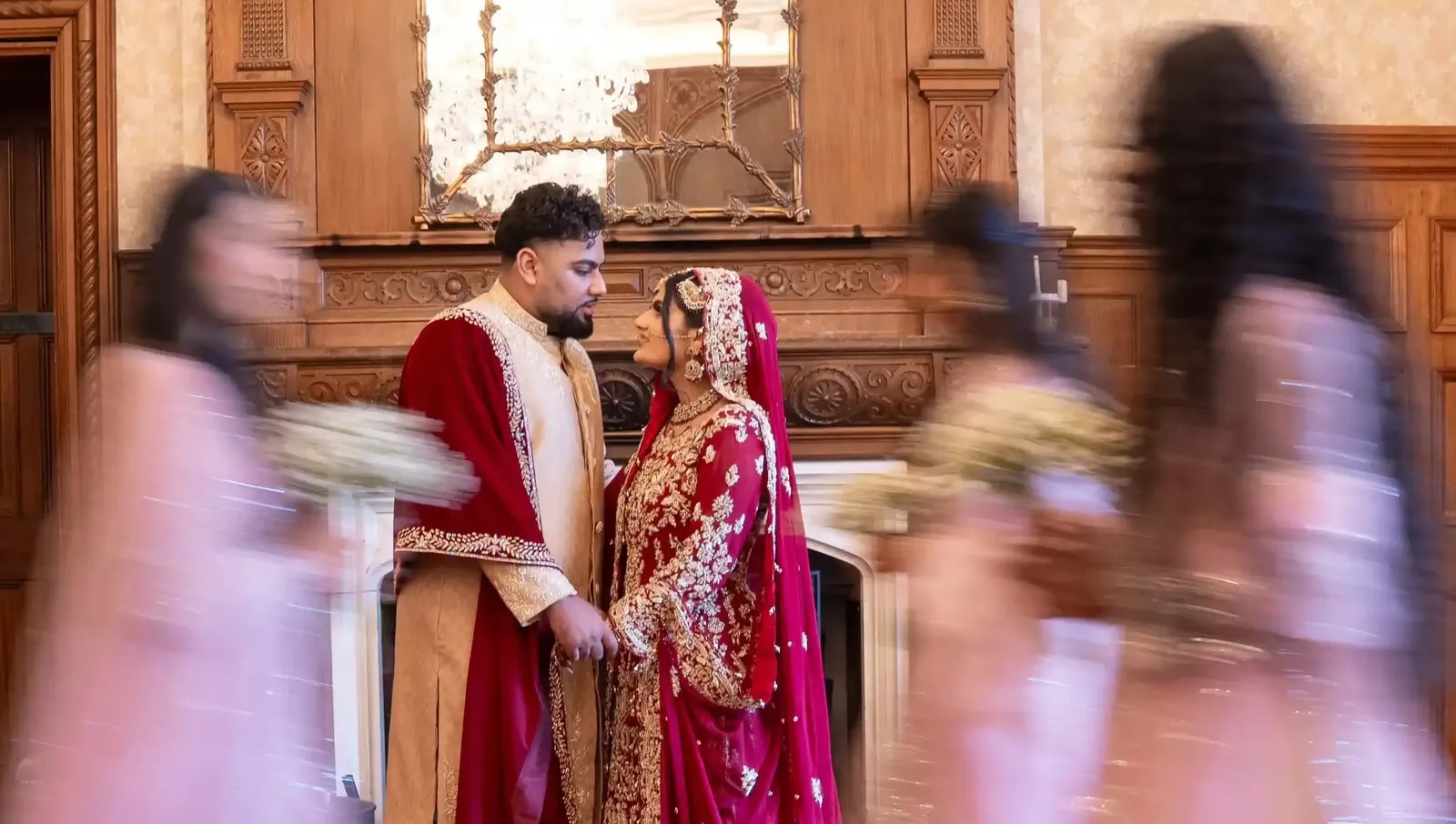 Bride and groom still in the doorway as her party in pink rushes past, blurred