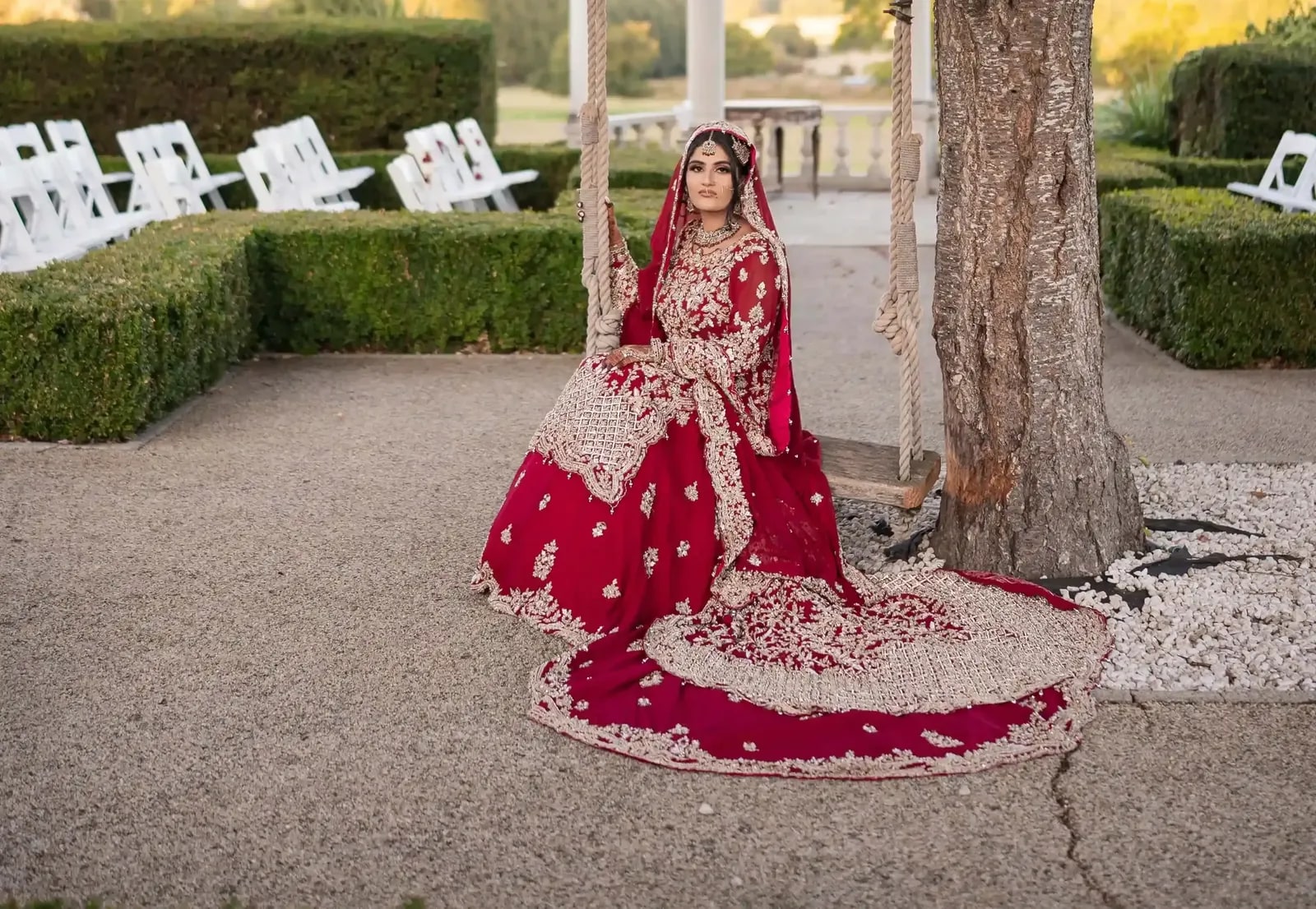 Bride on the swing beneath the tree at golden hour, her train laid across the gravel