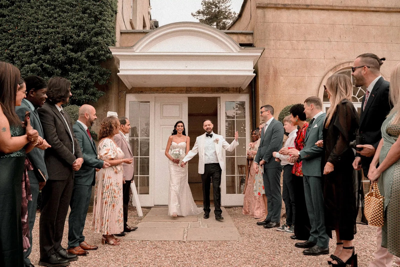 Bride and groom stepping out of the doorway between two lines of applauding guests