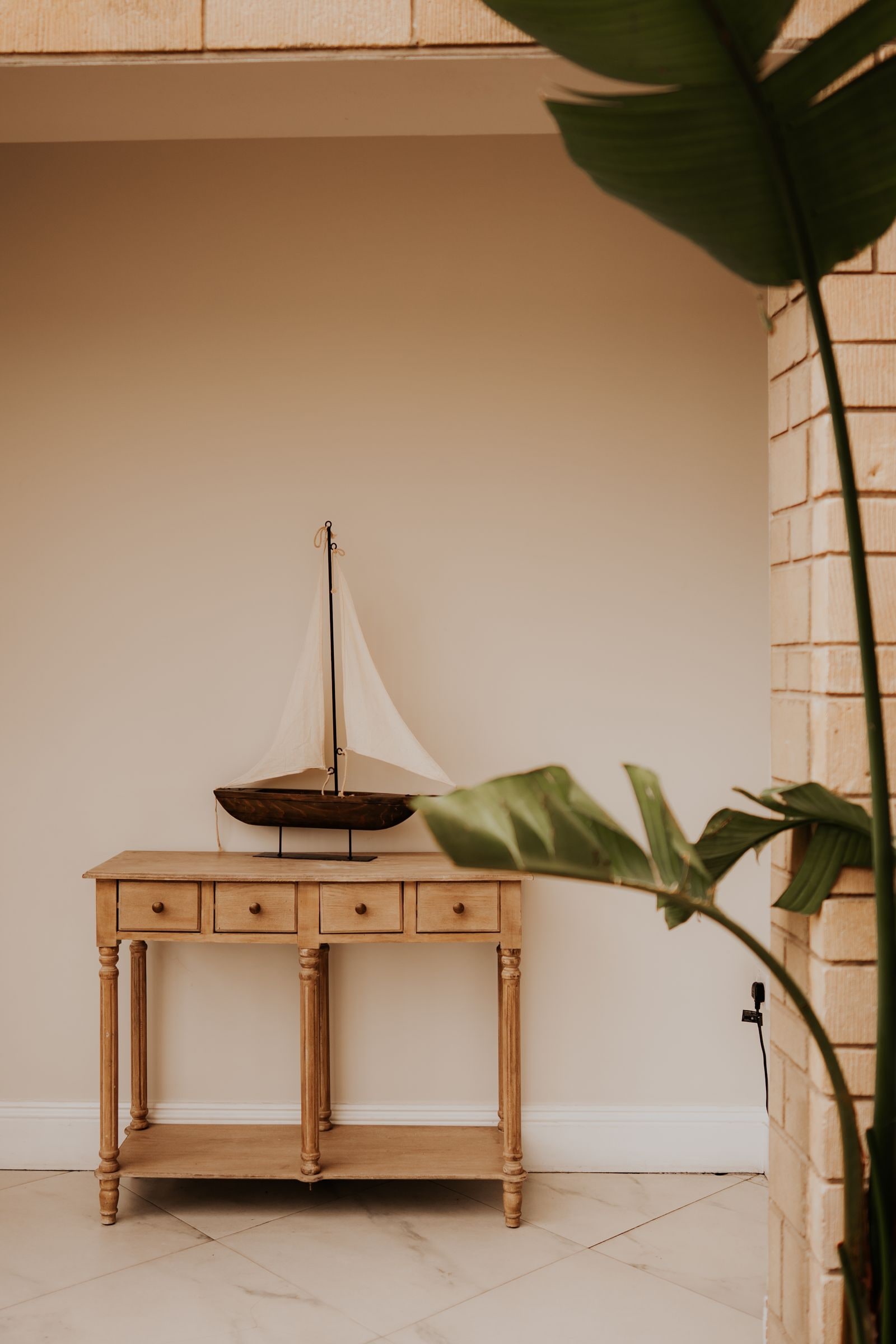 A model sailing boat on a console table beside a palm