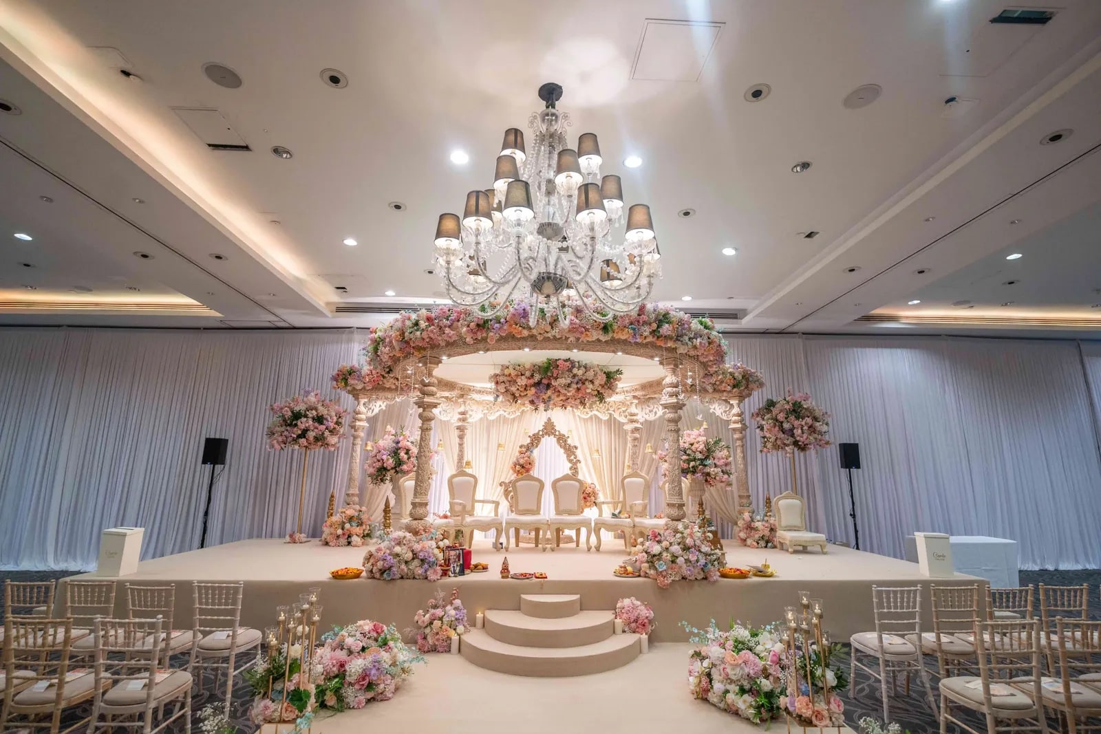 The empty hall before the ceremony, the flowered mandap lit under a chandelier