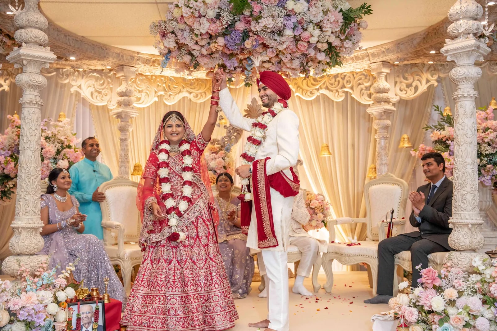 Groom raising his hand in triumph after the garland exchange, family watching